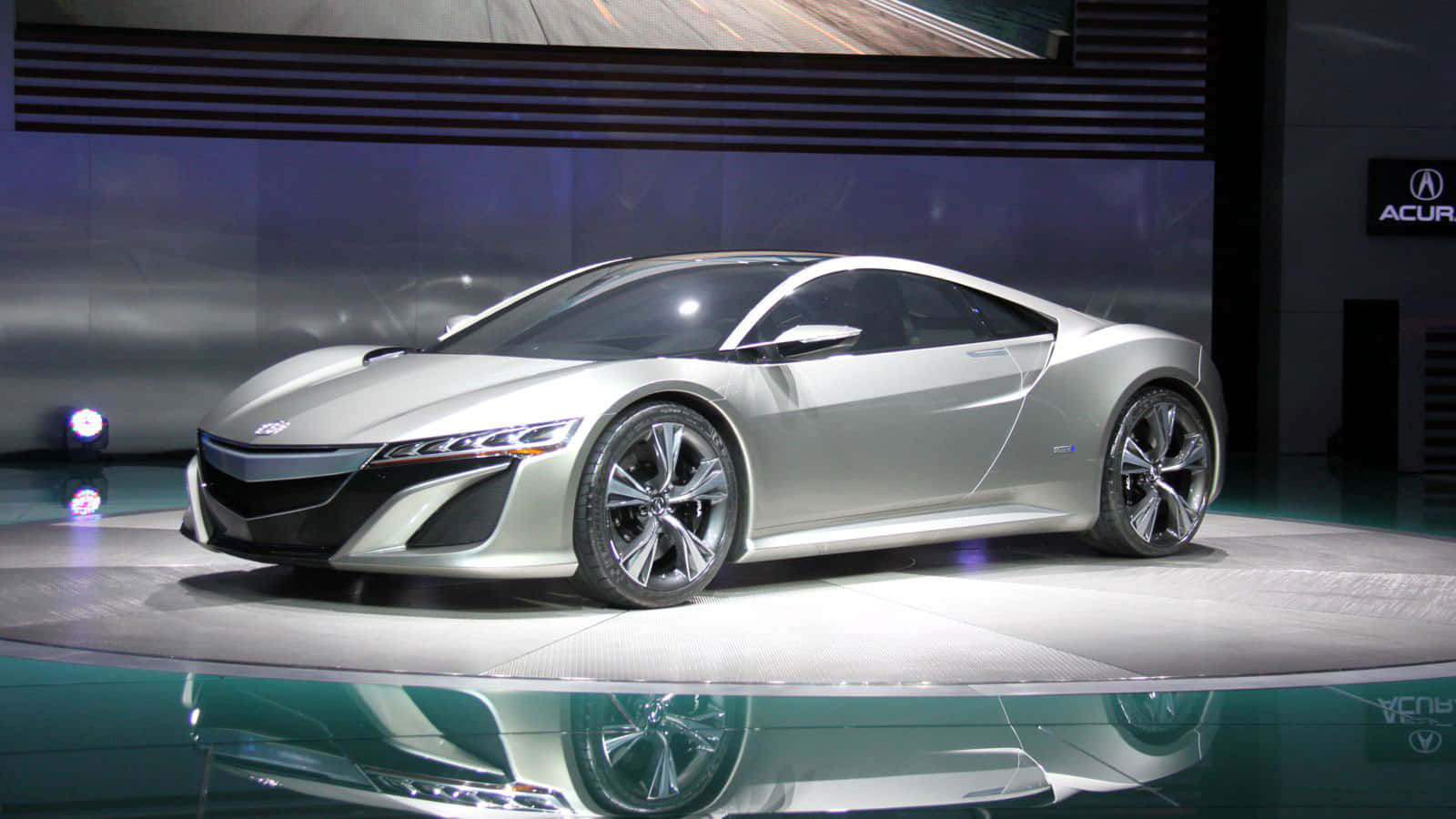 Acura 桌布 壁紙 — 一輛帶有黑色裝飾的時尚銀色跑車在車展的明亮聚光燈下展示在反光舞台上。