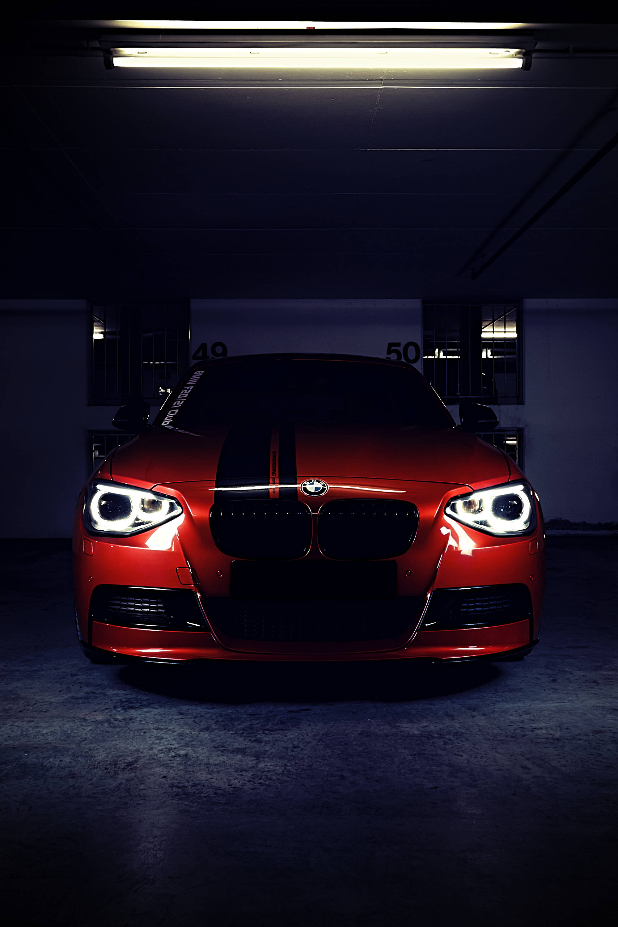 BMW M 桌布 壁紙 — 一輛帶有黑色賽車條紋的亮紅色BMW跑車，在昏暗的地下停車場中，在一盞螢光燈下直視前方。