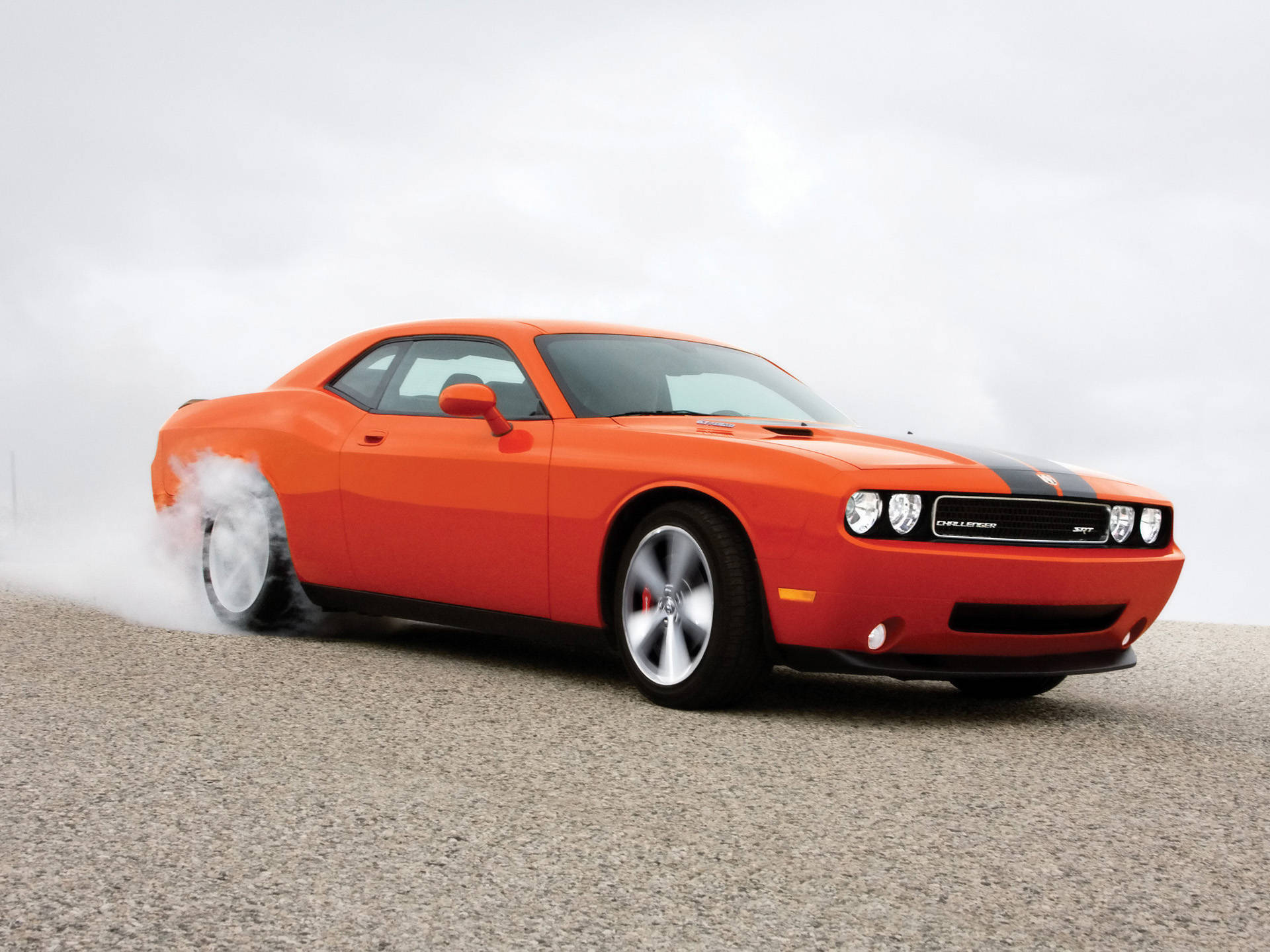Challenger 桌布 壁紙 — 一輛帶有黑色賽車條紋的充滿活力的橙色道奇挑戰者SRT，在多雲的天空下，在灰色瀝青路面上燒胎。