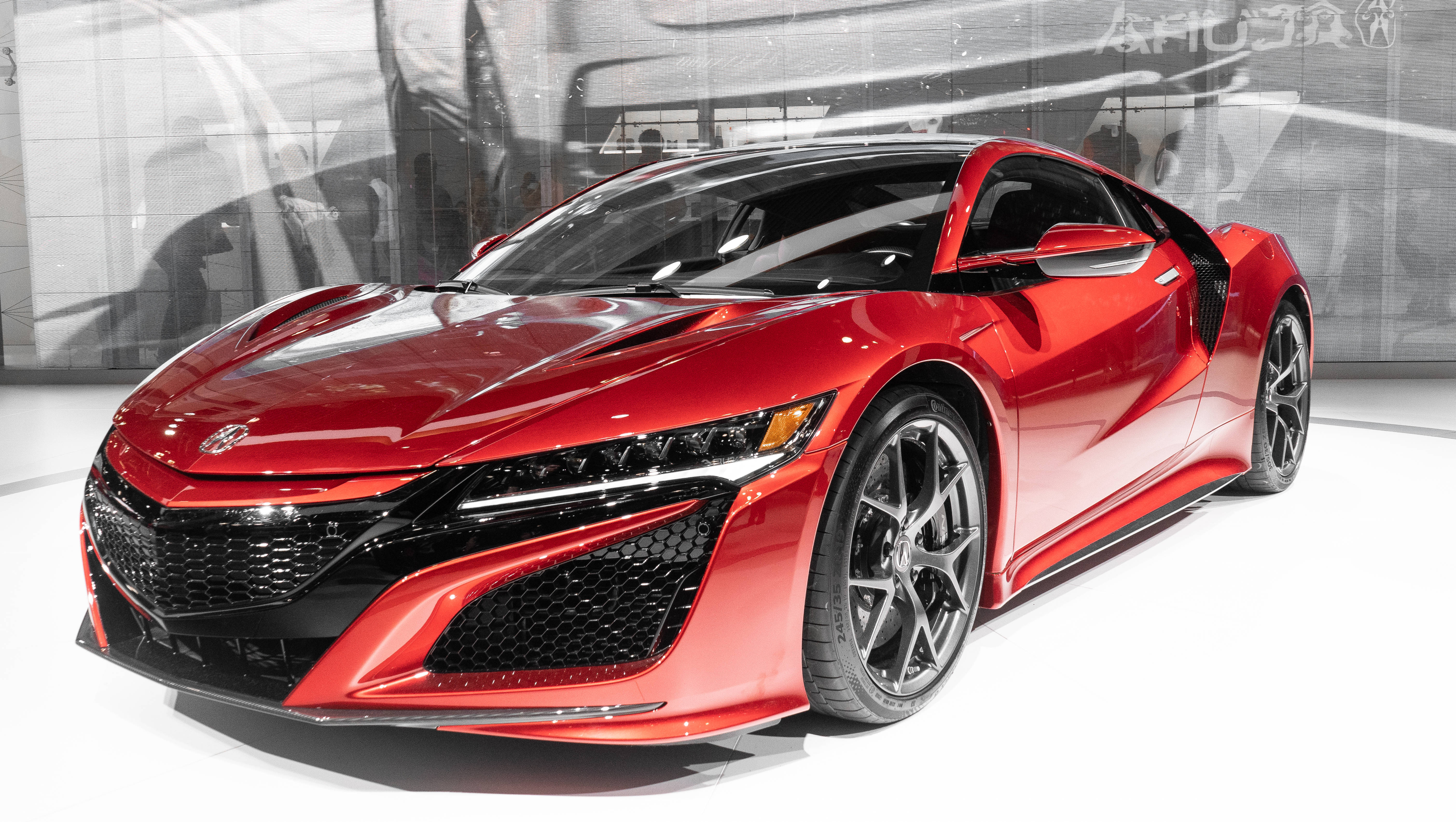 Acura 桌布 壁紙 — 一輛帶有黑色飾邊和時尚空氣動力學設計的亮紅色跑車，在明亮的燈光下展示在白色平台上。