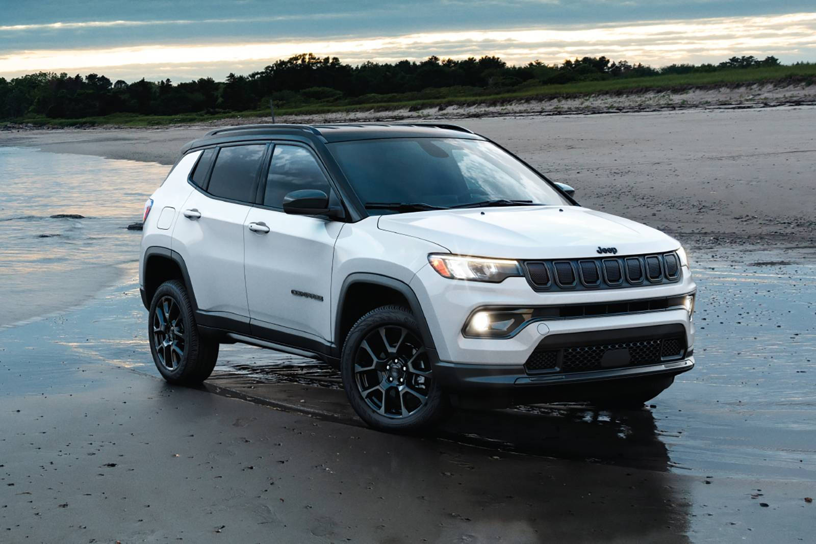 海灘 桌布 壁紙 — 一輛帶有黑色飾邊的白色Jeep Compass SUV停泊在黃昏時分的濕沙灘上，背景有樹木。