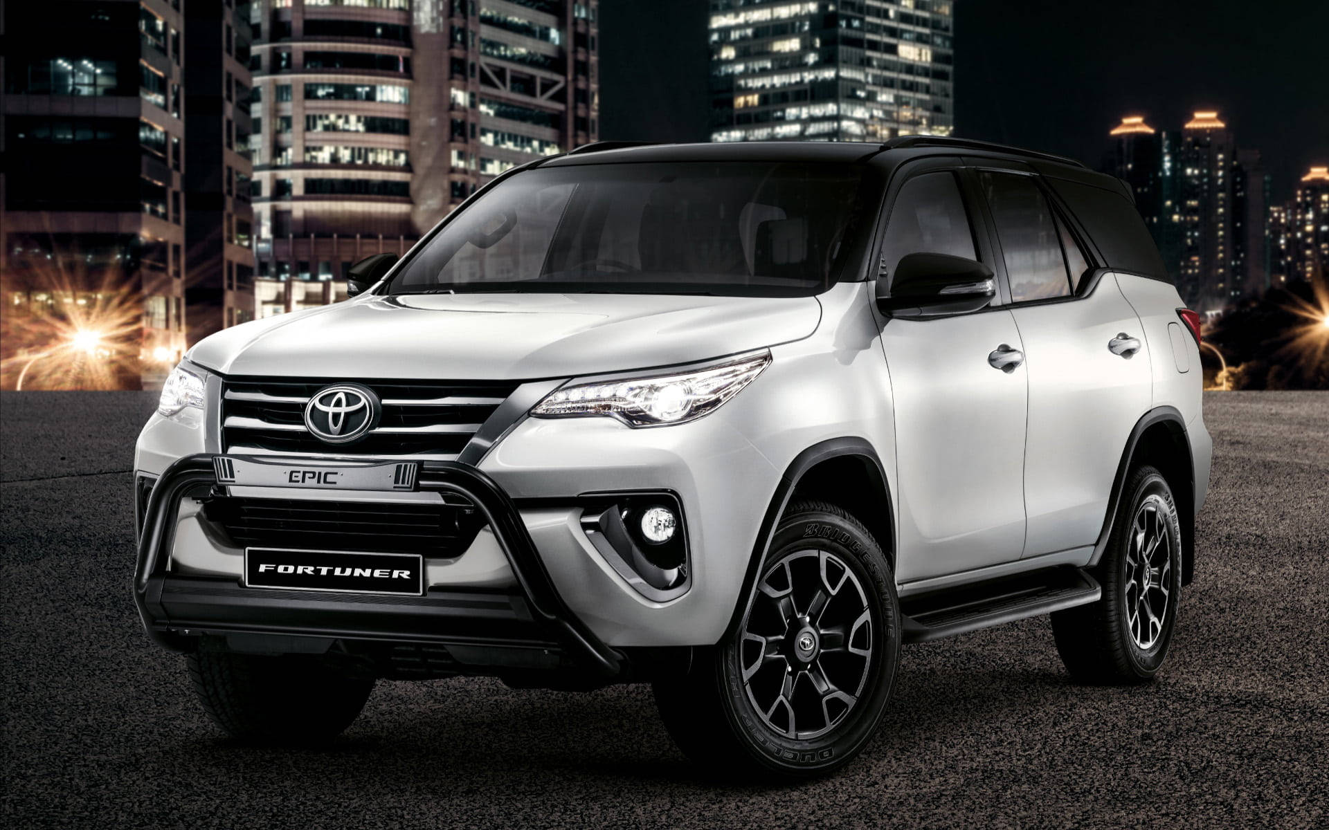 銀色豐田 Fortuner SUV 夜間停放在城市中，旁邊是明亮的建築物。 — Toyota Supra Mk4 壁紙