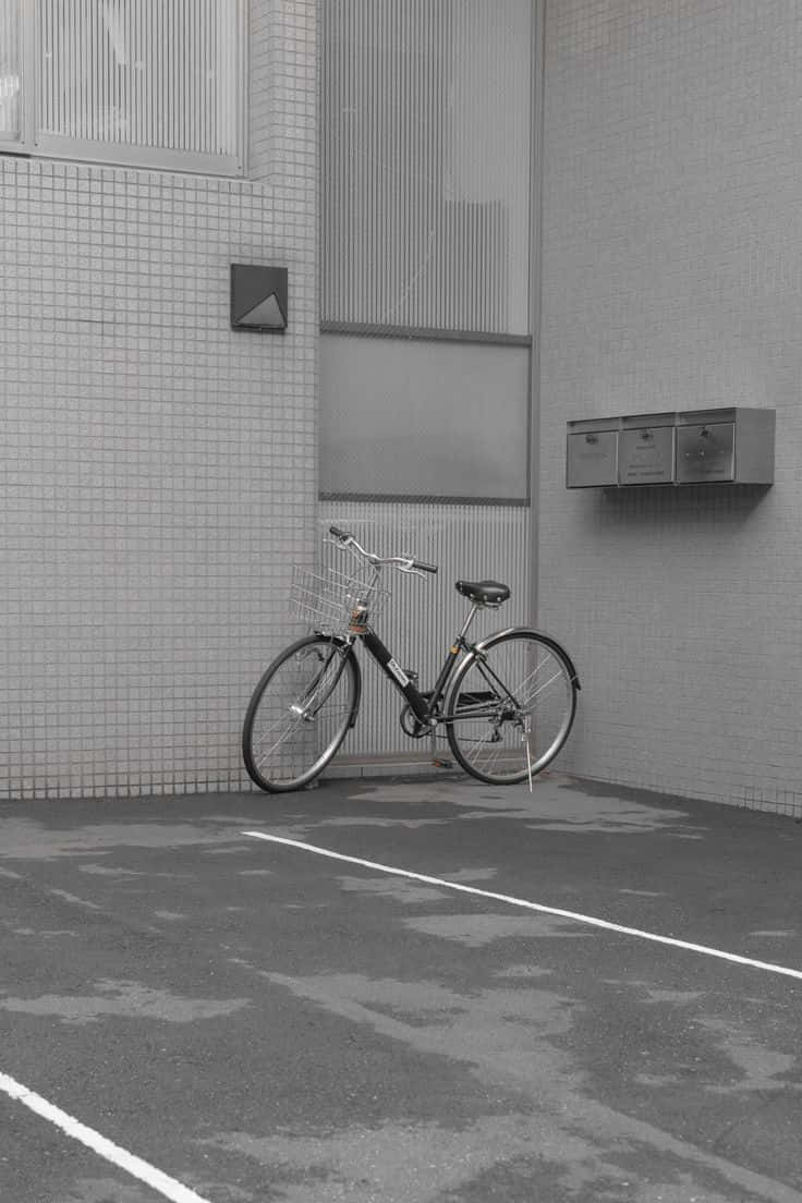 灰色美學動圖 桌布 壁紙 — 一輛帶籃子的孤獨腳踏車靠在瓷磚建築牆上，位於單色城市小巷中。