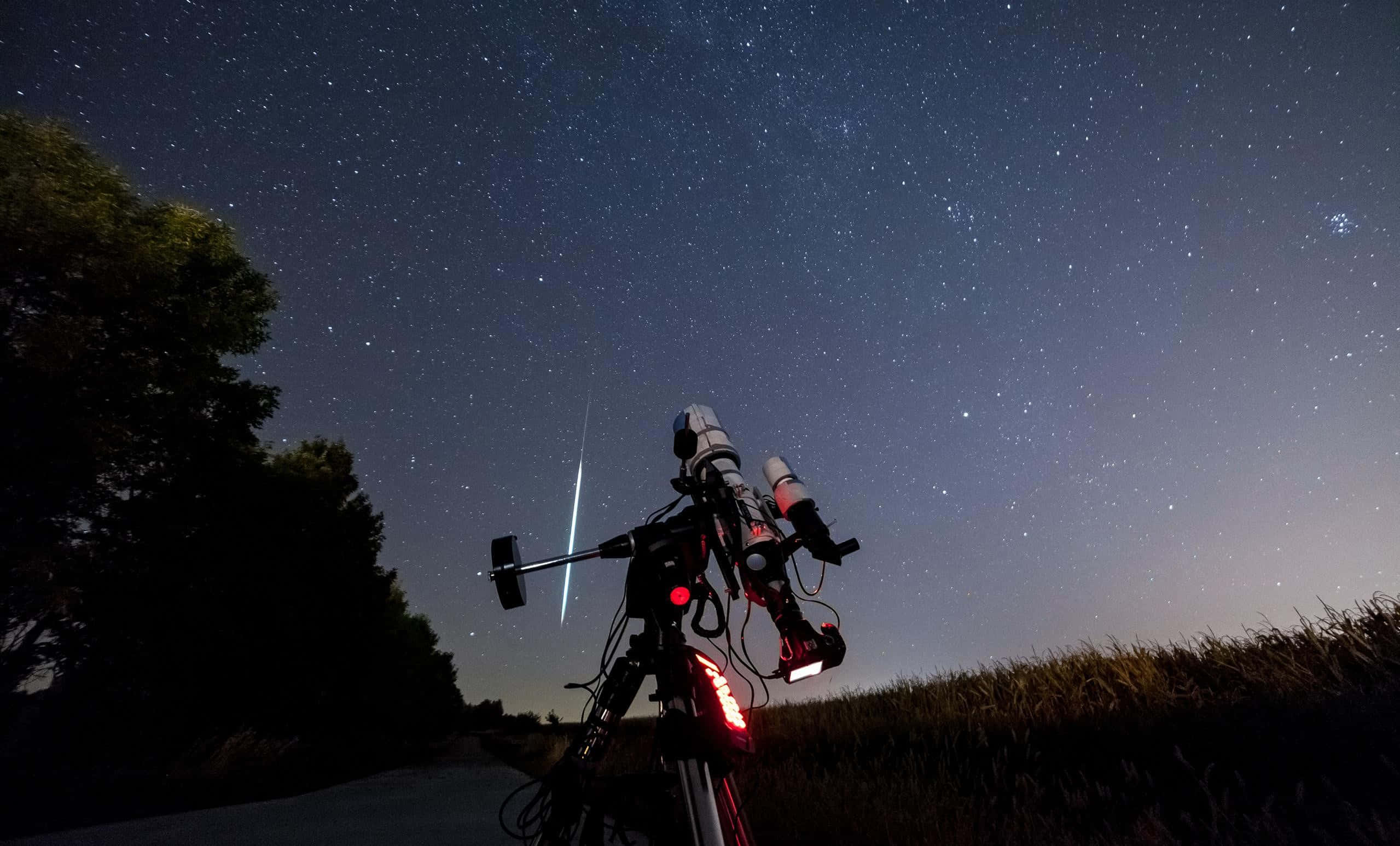 Telescope 桌布 壁紙 — 一輛帶紅燈的腳踏車停在鄉村道路上，上方是繁星點點的夜空，一顆明亮的流星劃過天際。