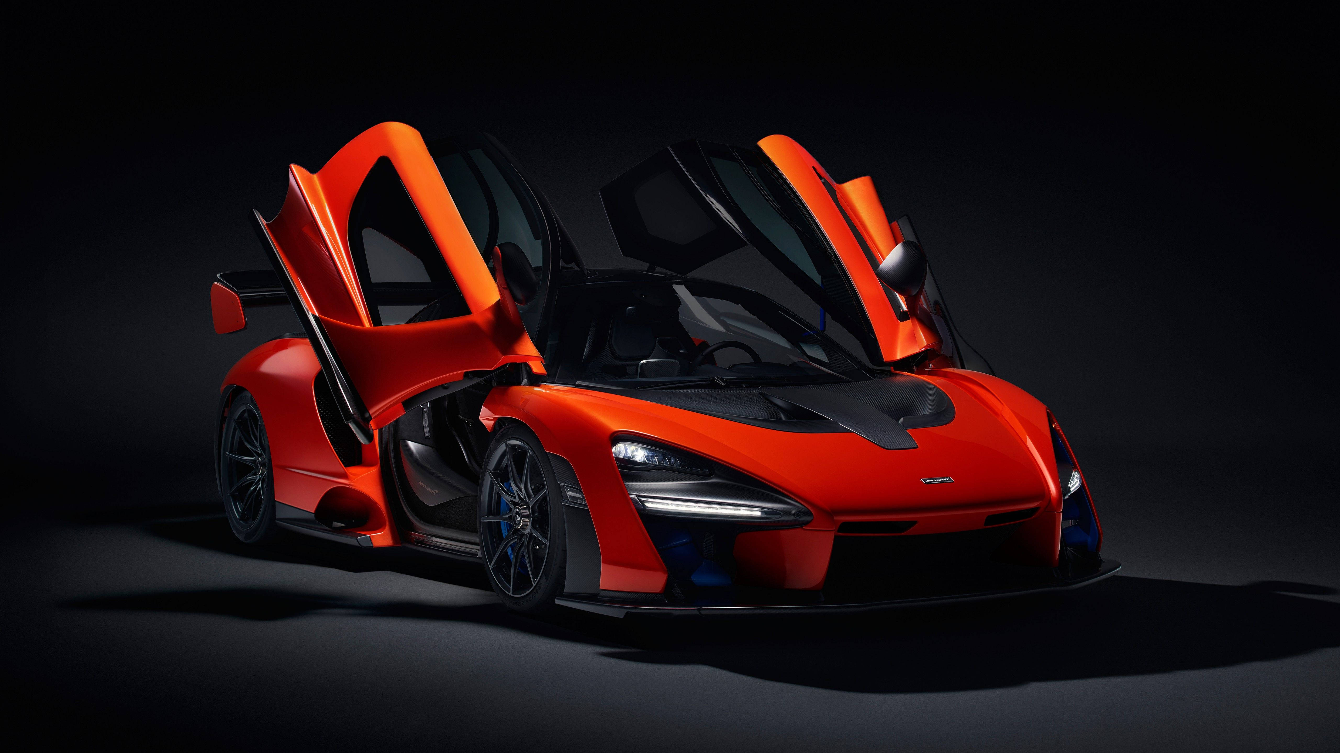 麥拉倫 桌布 壁紙 — 一輛引人注目的橙色McLaren Senna超級跑車，鷗翼門打開，在黑色背景下被戲劇性的工作室燈光照亮。