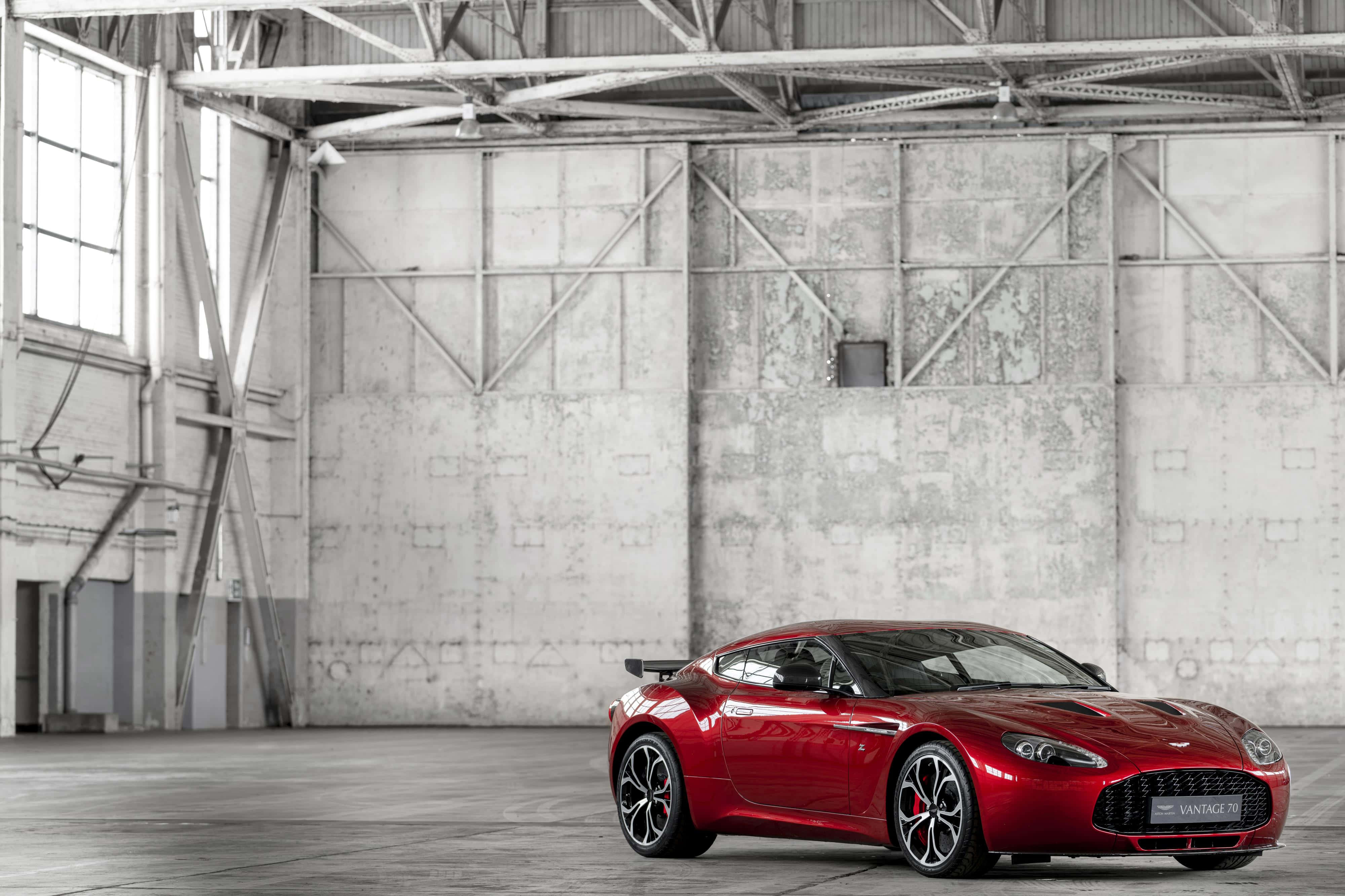 Aston Martin V12 Vantage 桌布 壁紙 — 一輛引人注目的紅色Aston Martin Vantage GTS在自然光下，於一個擁有裸露鋼樑和風化混凝土牆的寬敞工業倉庫內閃閃發光。