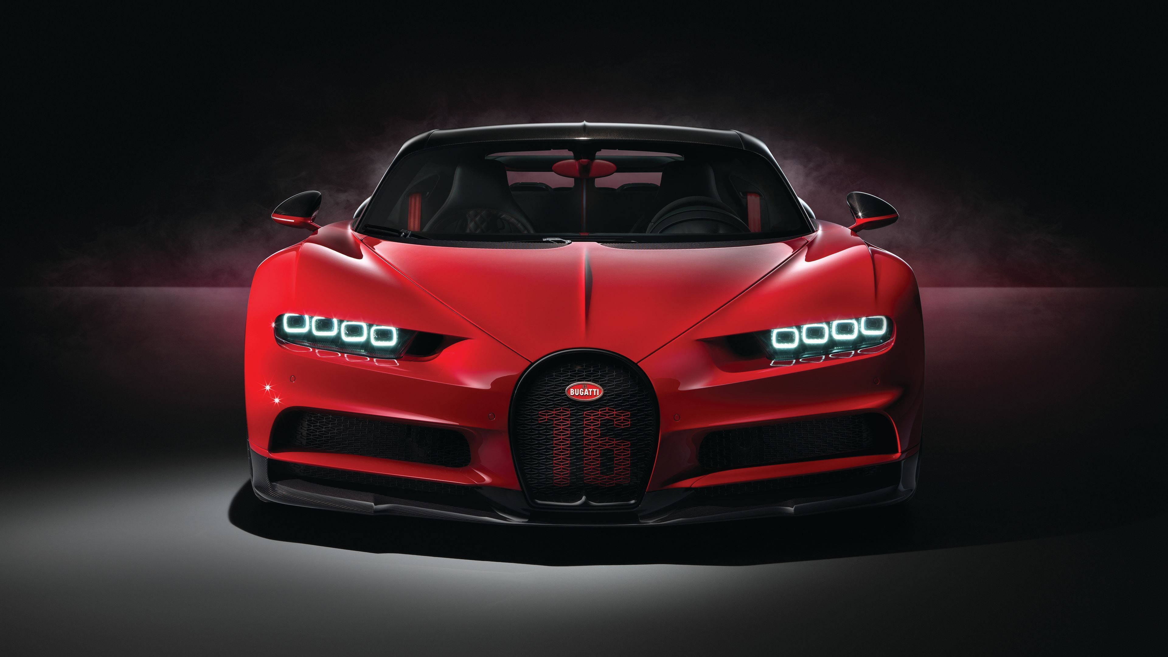 Cool Bugatti 桌布 壁紙 — 一輛引人注目的紅色Bugatti Chiron Super Sport 16，帶有發光的頭燈和「16」標誌，在黑暗的攝影棚背景下戲劇性地照亮。