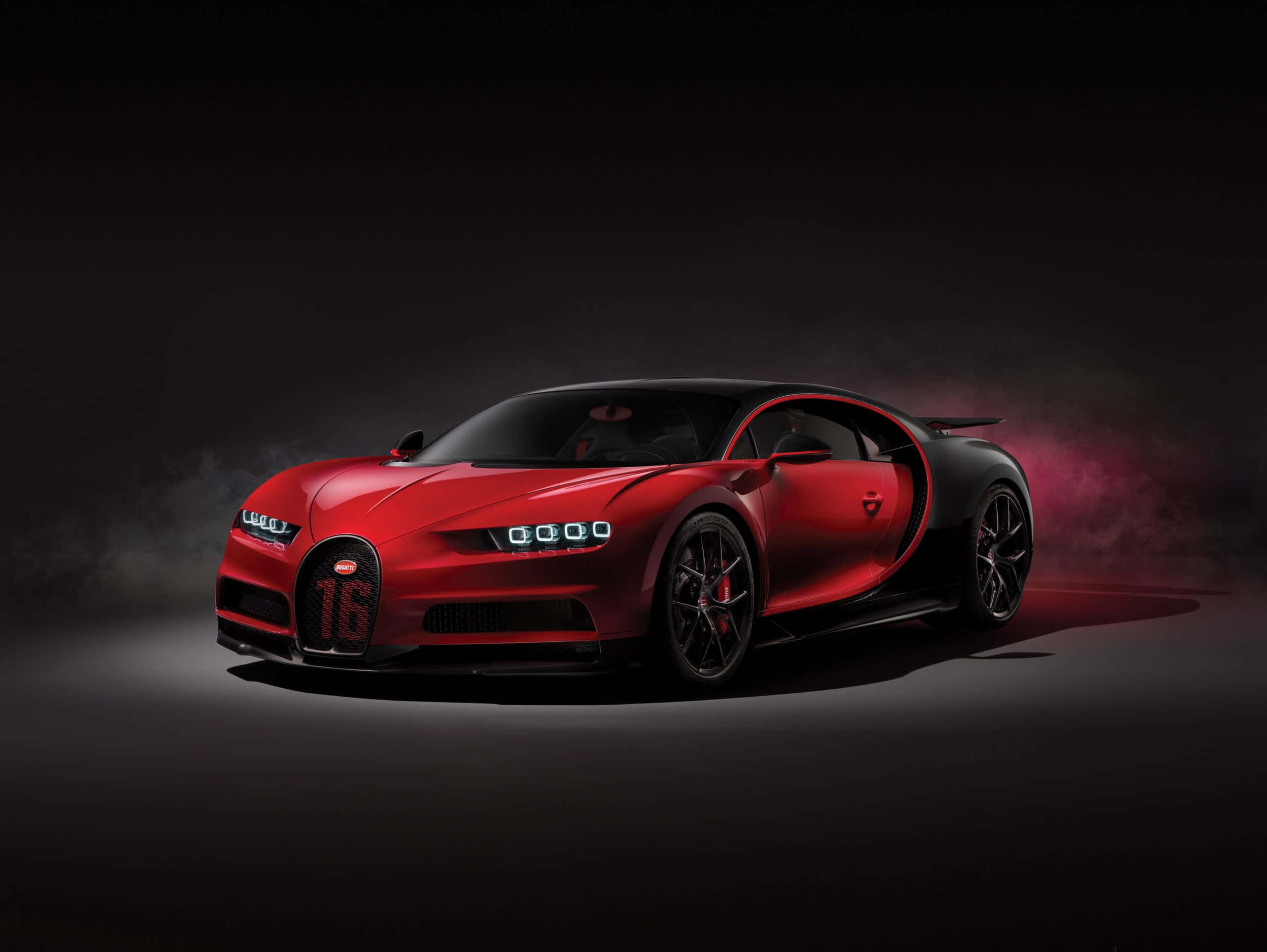 Best Bugatti 桌布 壁紙 — 一輛引人注目的紅色Bugatti Chiron，帶有黑色飾件和發光的車頭燈，戲劇性地站在黑暗煙霧背景前。