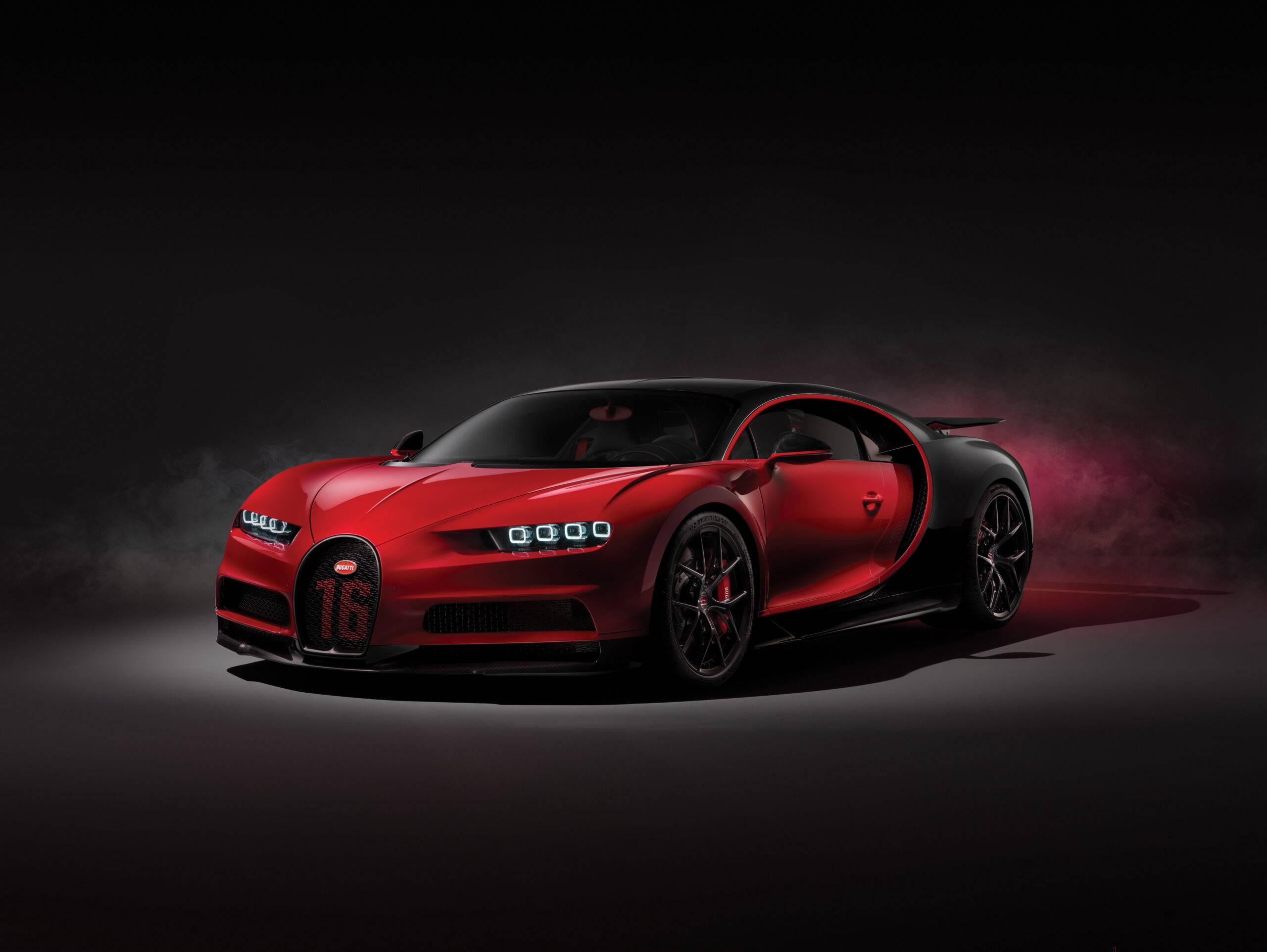 Cool Bugatti 桌布 壁紙 — 一輛引人注目的紅色Bugatti Chiron，帶有黑色飾邊和發光的車頭燈，在黑暗的攝影棚背景中與粉紅色的煙霧形成戲劇性的對比。