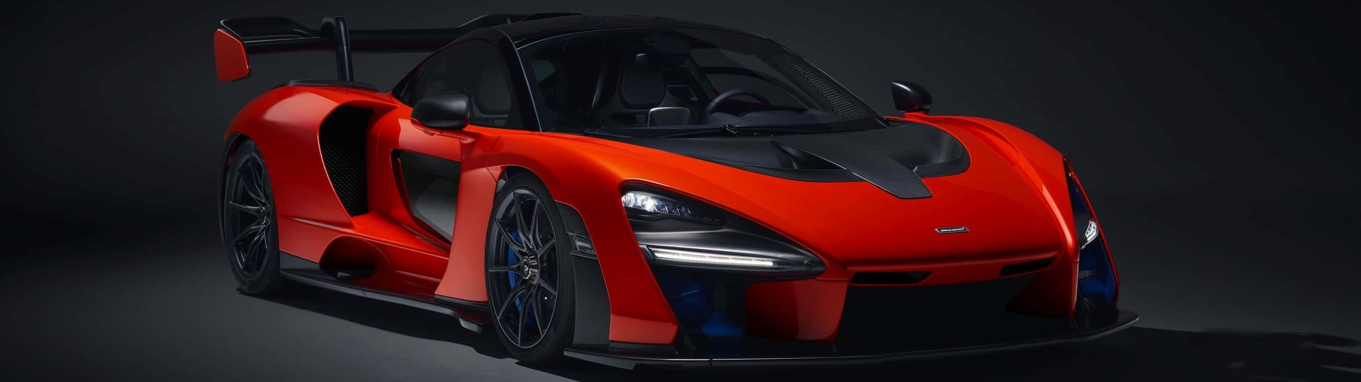 紅色McLaren Senna超級跑車，帶有黑色飾件和藍色煞車卡鉗，在攝影棚燈光下。 — 超寬 GIF 壁紙