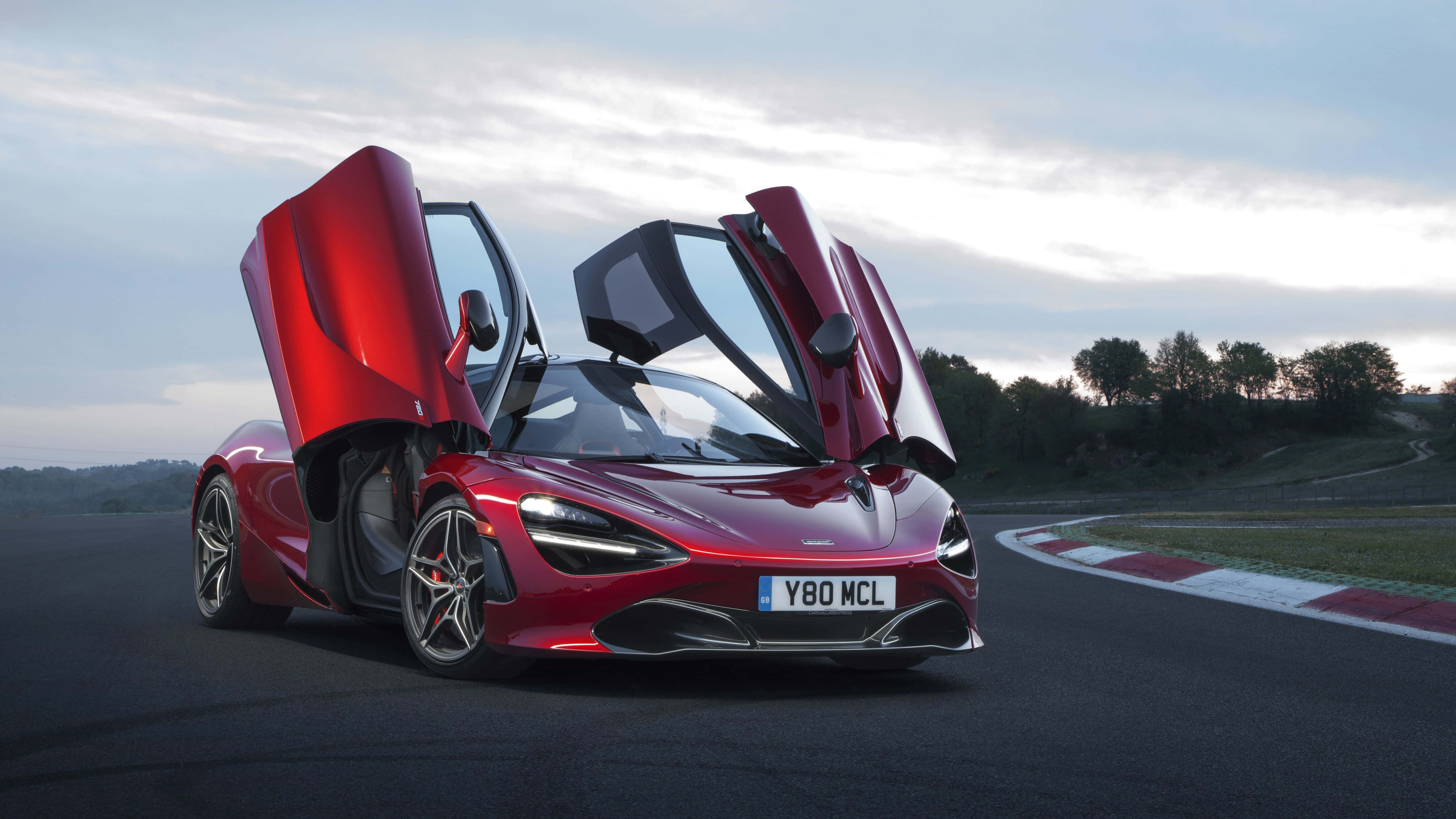 Mclaren 720s 桌布 壁紙 — 一輛引人注目的紅色McLaren跑車在賽道上打開鷗翼車門，時值黃昏。