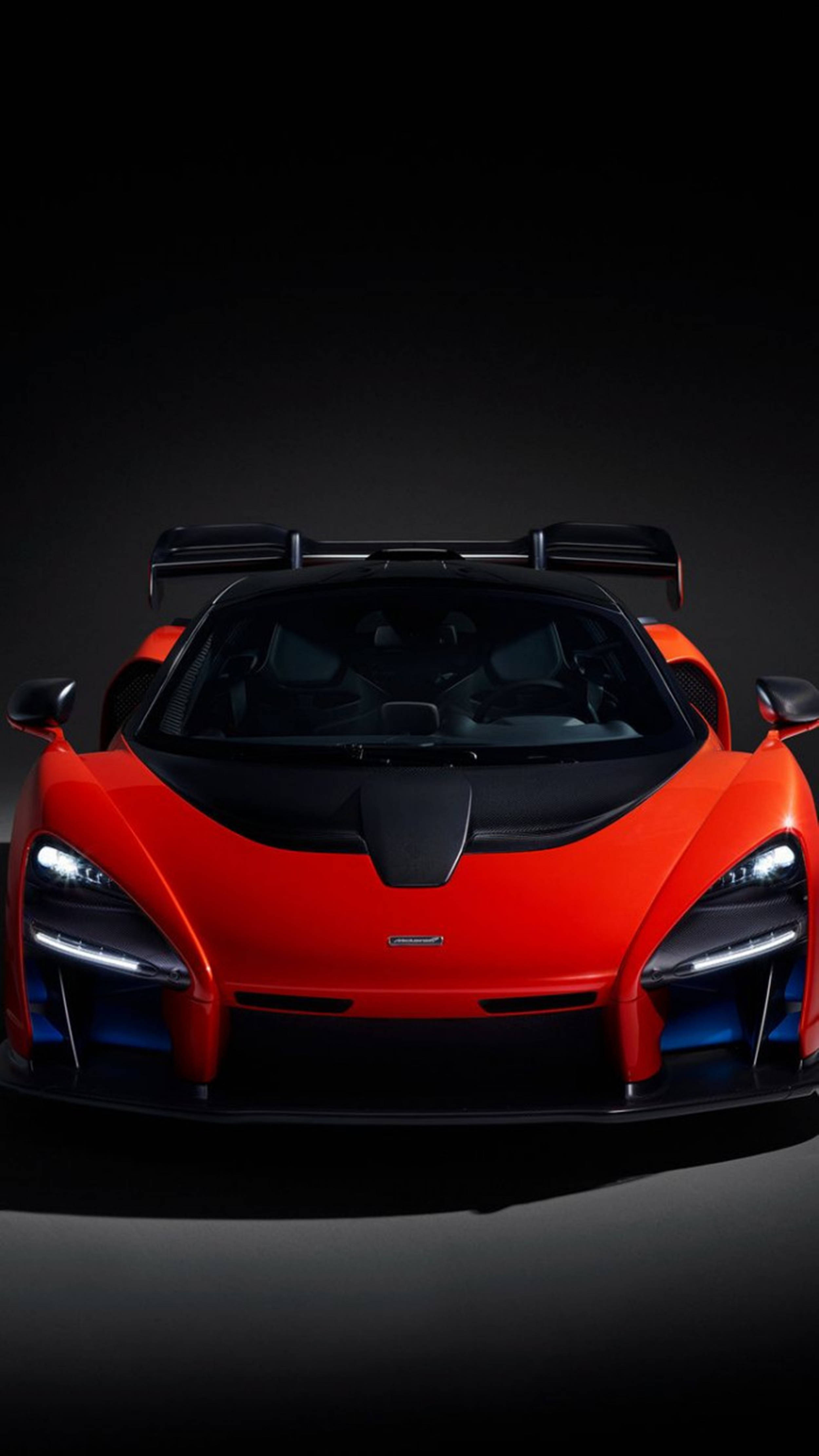 Luxury 桌布 壁紙 — 一輛引人注目的紅色McLaren Senna跑車，配備發光的頭燈和黑色尾翼，從正面在深色工作室背景前拍攝。