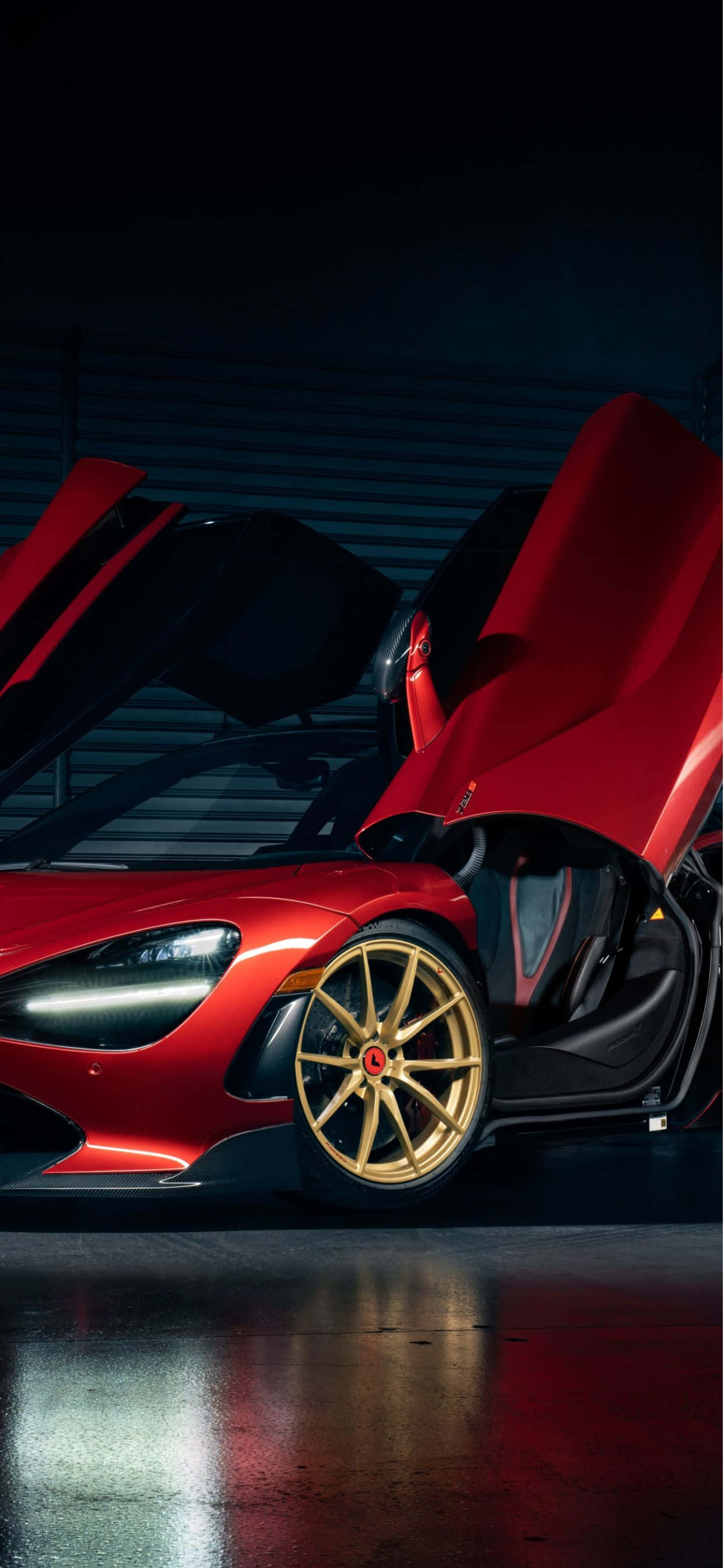 紅色動圖 桌布 壁紙 — 一輛引人注目的紅色McLaren跑車，配備金色輪圈和打開的蝴蝶門，在黑暗車庫的戲劇性燈光下閃閃發光。