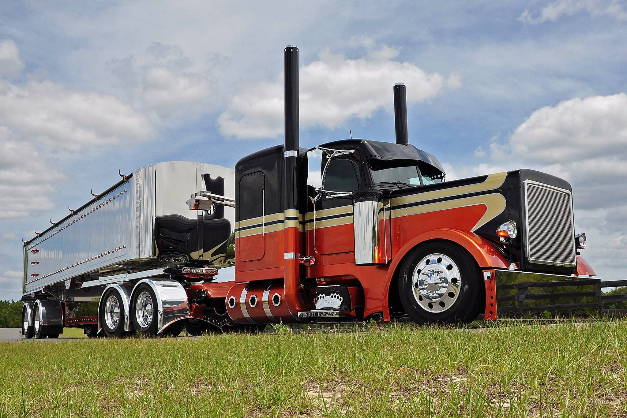 Peterbilt 桌布 壁紙 — 一輛引人注目的紅色和黑色定制半掛卡車，帶有鍍鉻裝飾，停在草地上，天空部分多雲。
