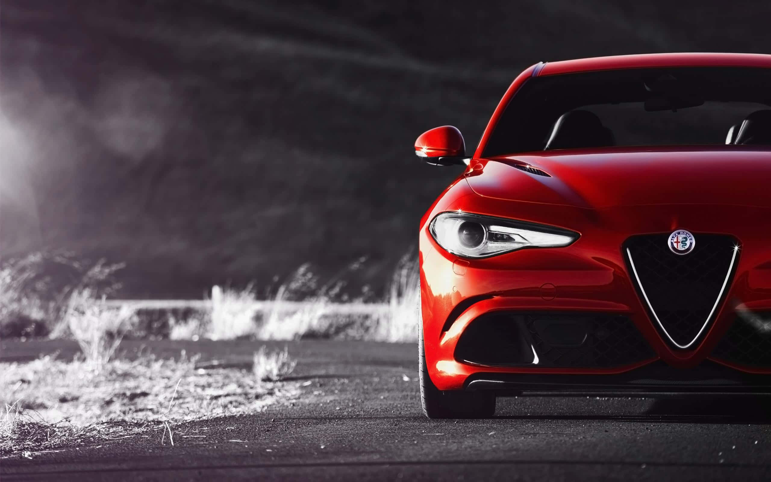 Alfa Romeo Giulia 桌布 壁紙 — 一輛引人注目的紅色愛快羅密歐跑車在昏暗道路上的戲劇性燈光下閃閃發光，背景迷濛。