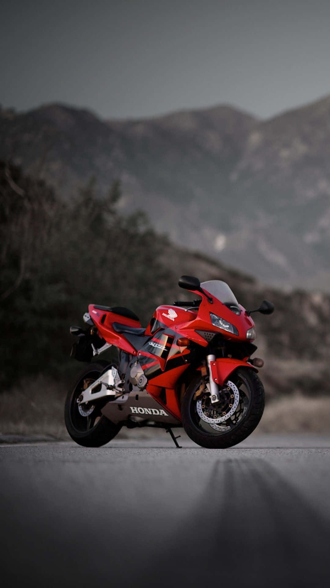 Motorcycle iPhone 桌布 壁紙 — 一輛引人注目的紅色本田跑車摩托車停在空蕩的道路上，背景是霧濛濛的山巒。