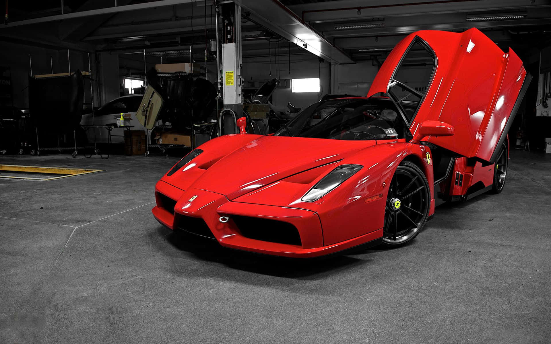 Ferrari Enzo 桌布 壁紙 — 一輛引人注目的紅色法拉利Enzo，其標誌性剪刀門敞開，停放在燈光昏暗的工業車庫中。