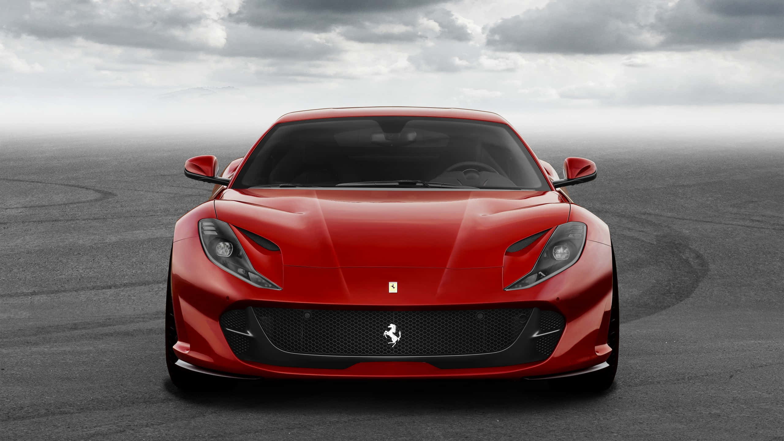 Ferrari Portofino 桌布 壁紙 — 一輛引人注目的紅色法拉利跑車在灰色瀝青賽道上朝前，天空多雲。