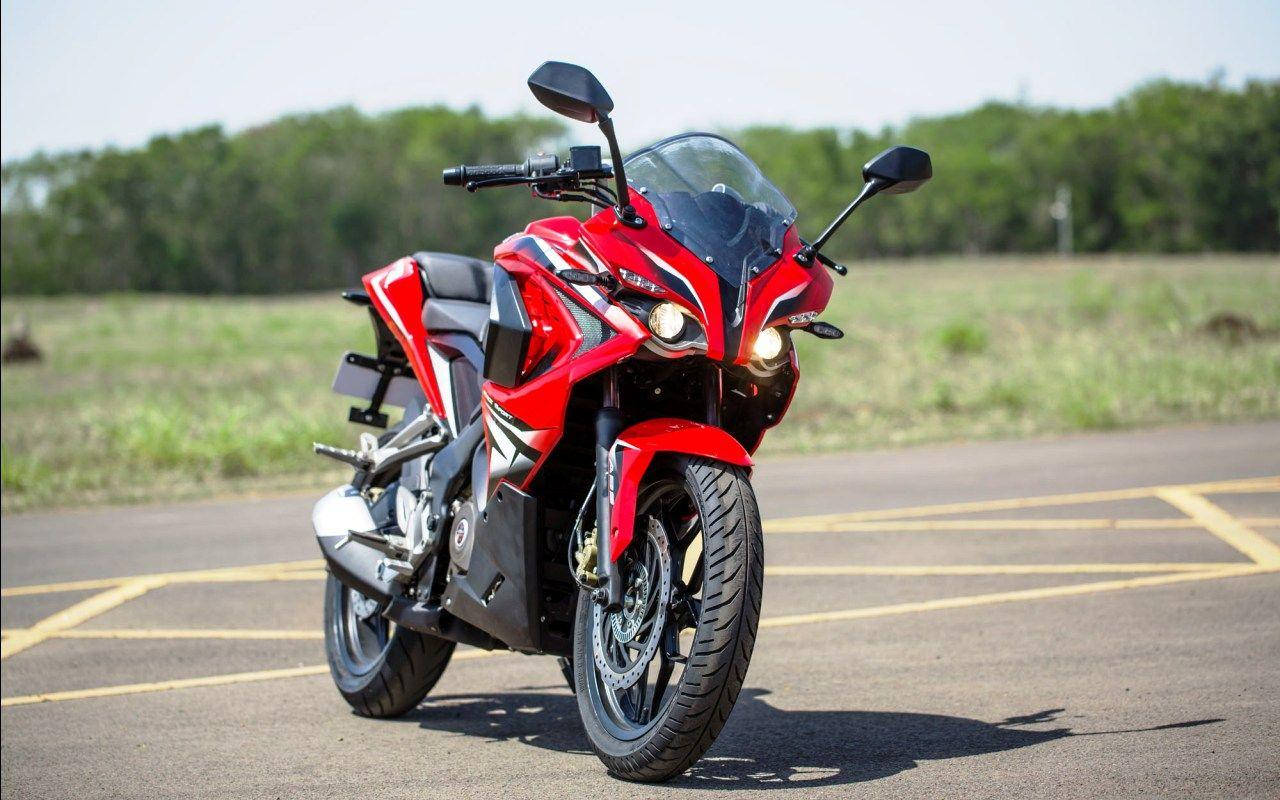 Racing 桌布 壁紙 — 一輛引人注目的紅色運動機車，頭燈發亮，停放在明亮的日光下的瀝青停車場。