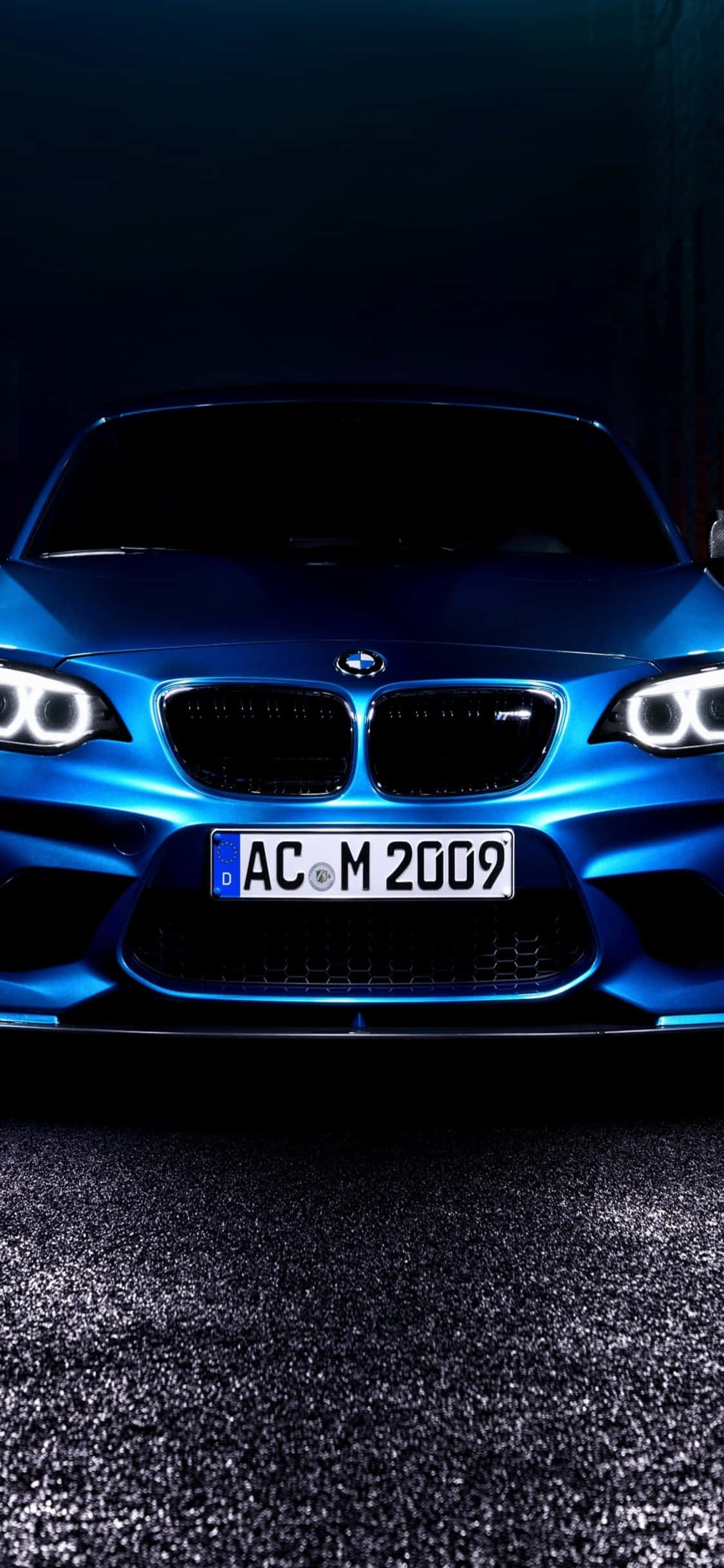 iPhone X Bmw 桌布 壁紙 — 一輛引人注目的藍色BMW M2跑車在戲劇性燈光下，在帶有反射瀝青的黑暗背景中閃耀。