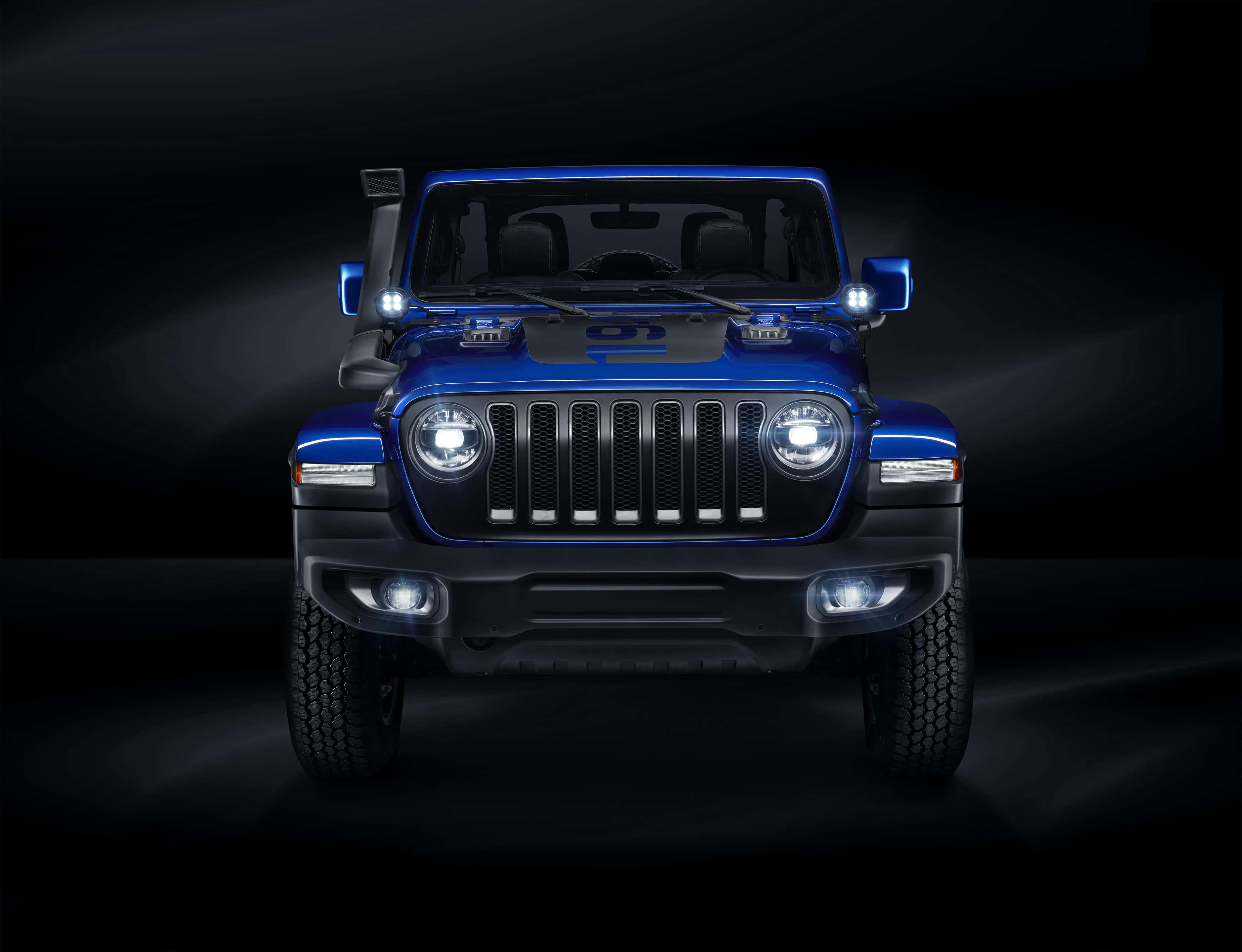Jeep Liberty 桌布 壁紙 — 一輛引人注目的藍色Jeep Wrangler在黑暗的攝影棚環境中，車頭燈閃耀，向黑色背景投射出戲劇性的光束。