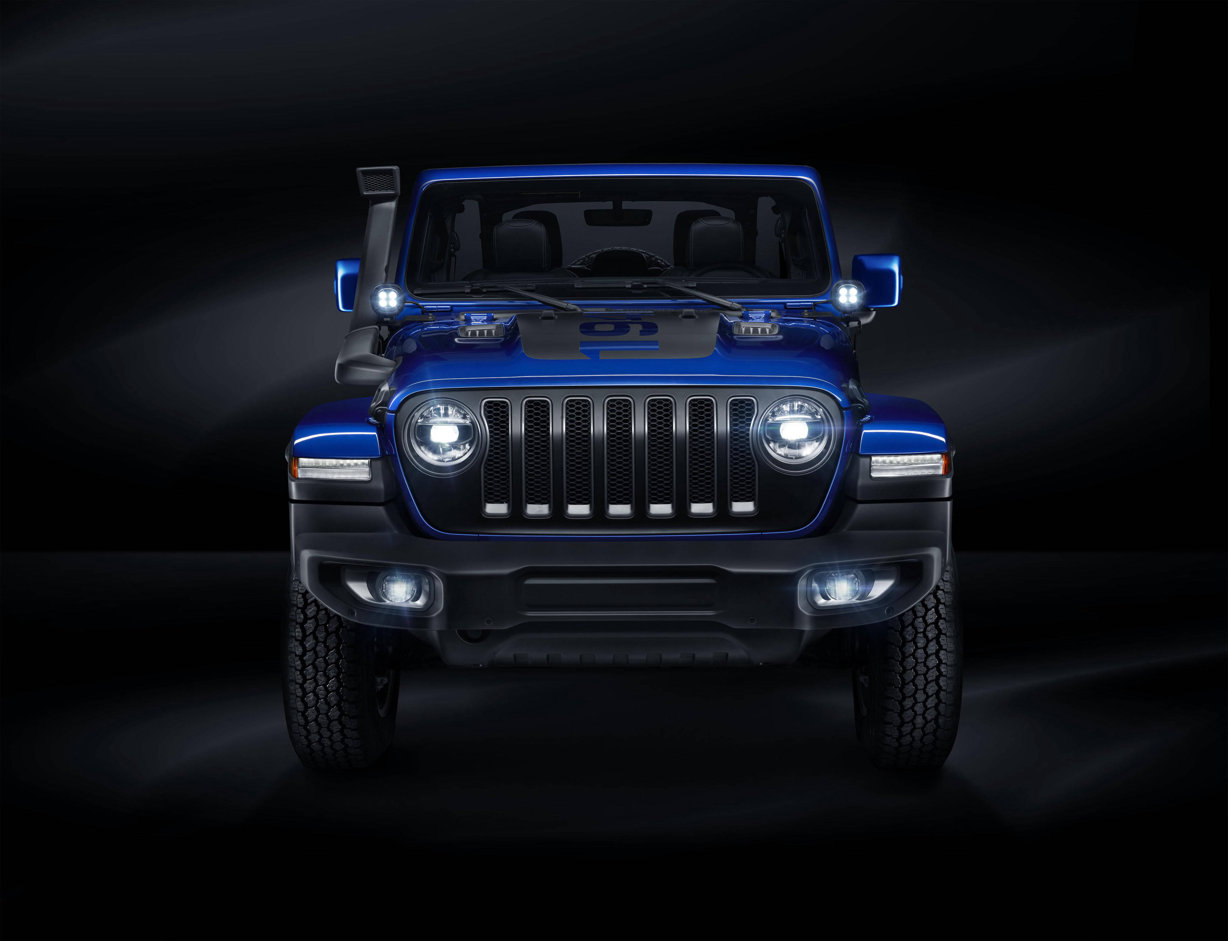 Mopar 桌布 壁紙 — 一輛引人注目的藍色Jeep Wrangler，車頭燈閃爍，在黑暗的攝影棚環境中佔據主導地位，散發出力量和粗獷的優雅。
