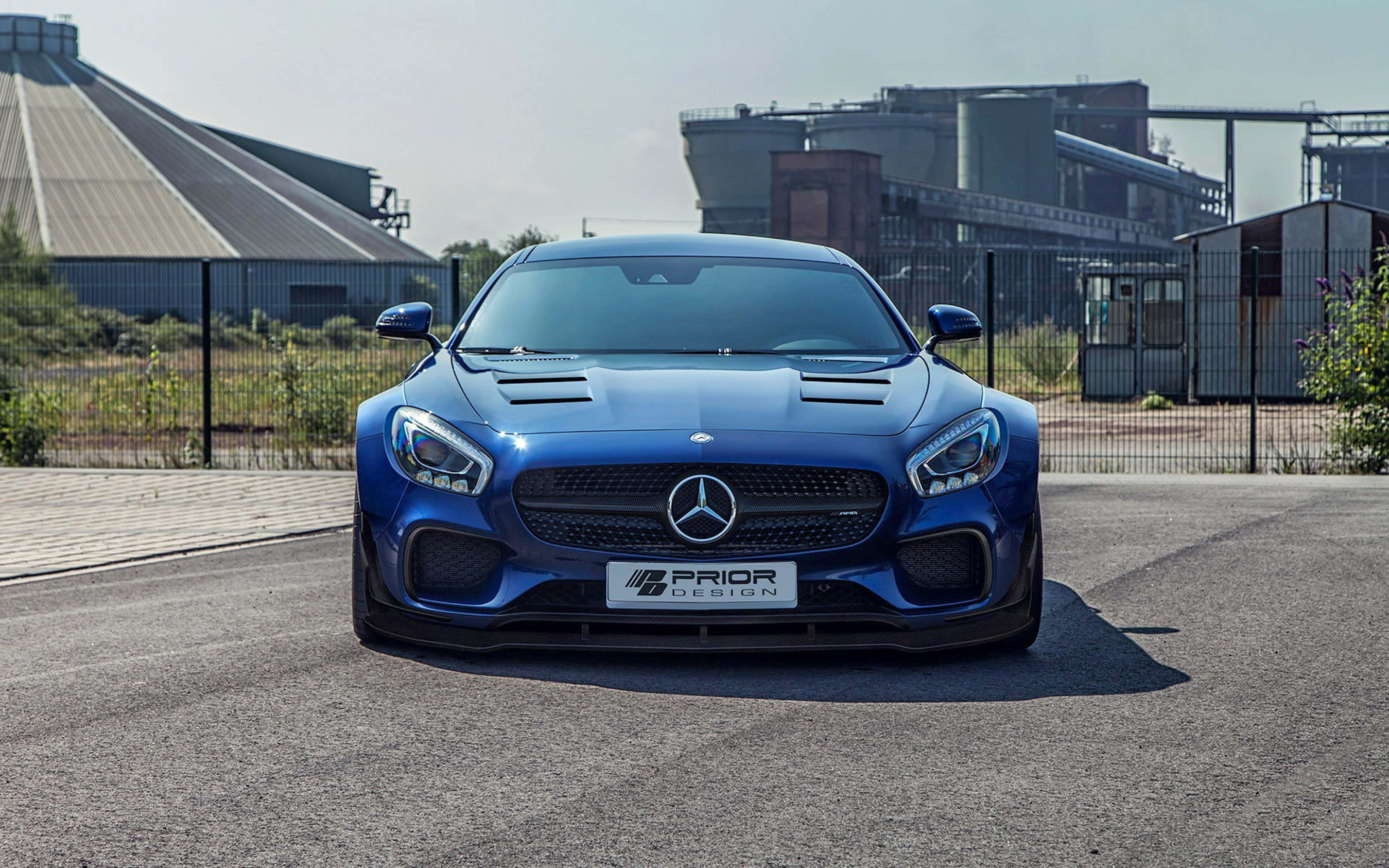藍色 桌布 壁紙 — 一輛引人注目的藍色Mercedes-AMG GT S，配備Prior Design改裝，在明亮的日光下停在工業綜合體前的瀝青路面上。