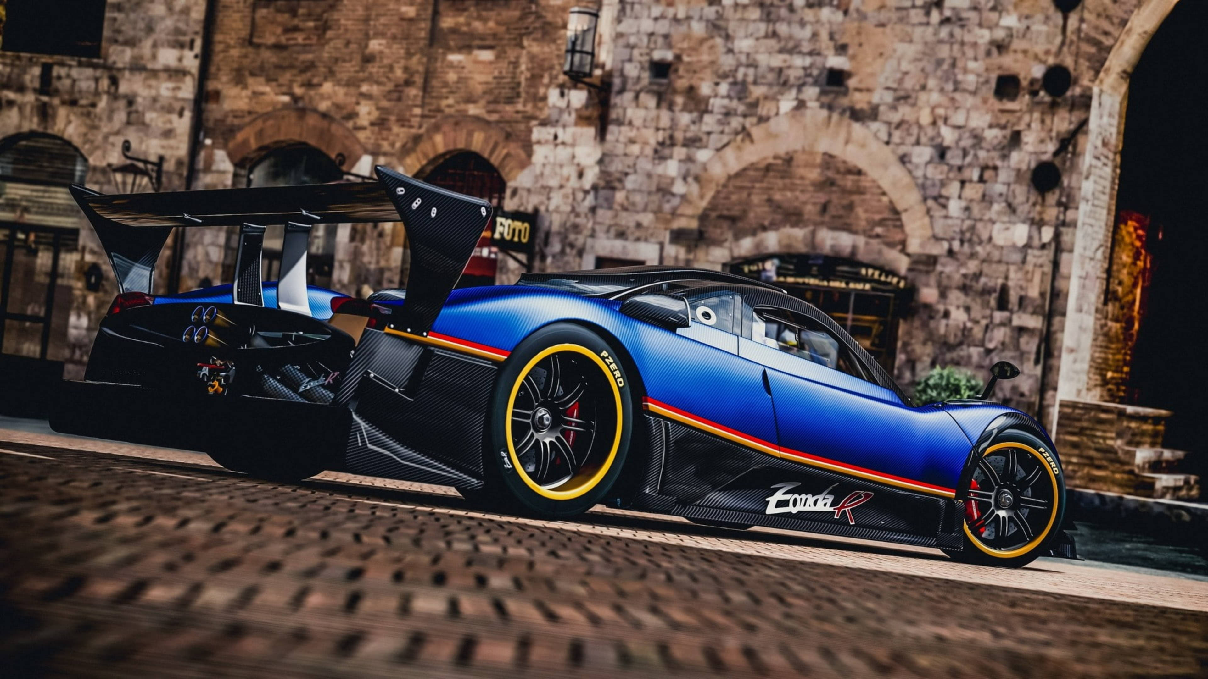 帕加尼 桌布 壁紙 — 一輛引人注目的藍色Pagani Zonda R超跑，配備黃色輪圈，停放在歷史石建築前的鵝卵石路上。