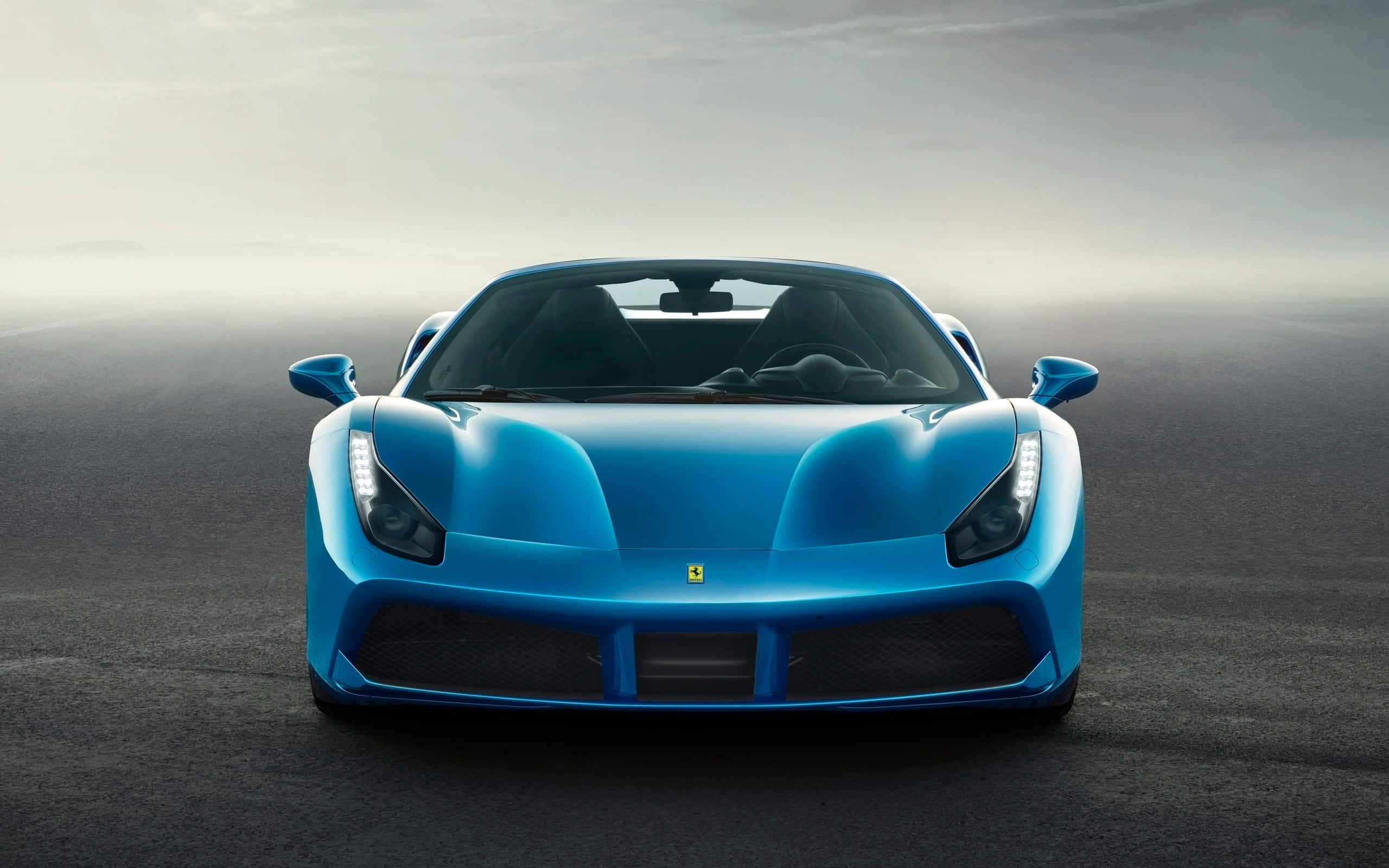 Ferrari 488 Spider 桌布 壁紙 — 一輛引人注目的藍色法拉利跑車在陰天下的霧濛濛灰色瀝青路上向前行駛。