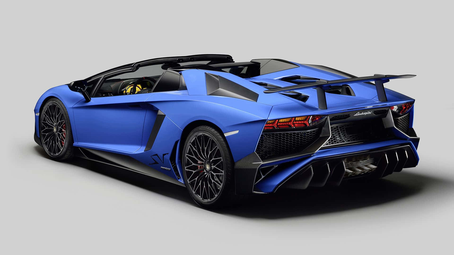 跑車 桌布 壁紙 — 一輛引人注目的藍色藍寶堅尼Aventador SVJ Roadster，帶有黑色飾件和紅色制動卡鉗，從後方四分之三角度展示在純灰色背景前。