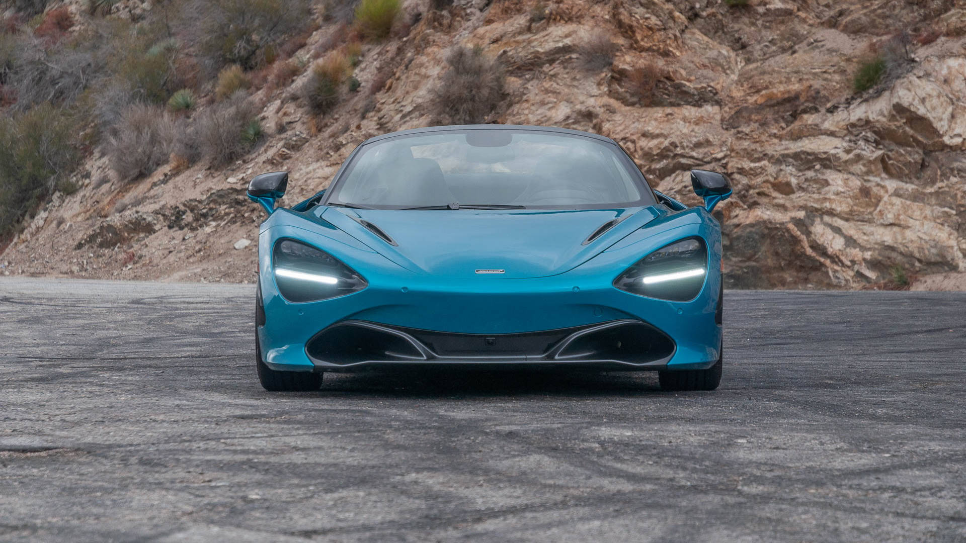 跑車 桌布 壁紙 — 一輛引人注目的青綠色McLaren 720S跑車在崎嶇的瀝青路上正面朝向岩石山坡。