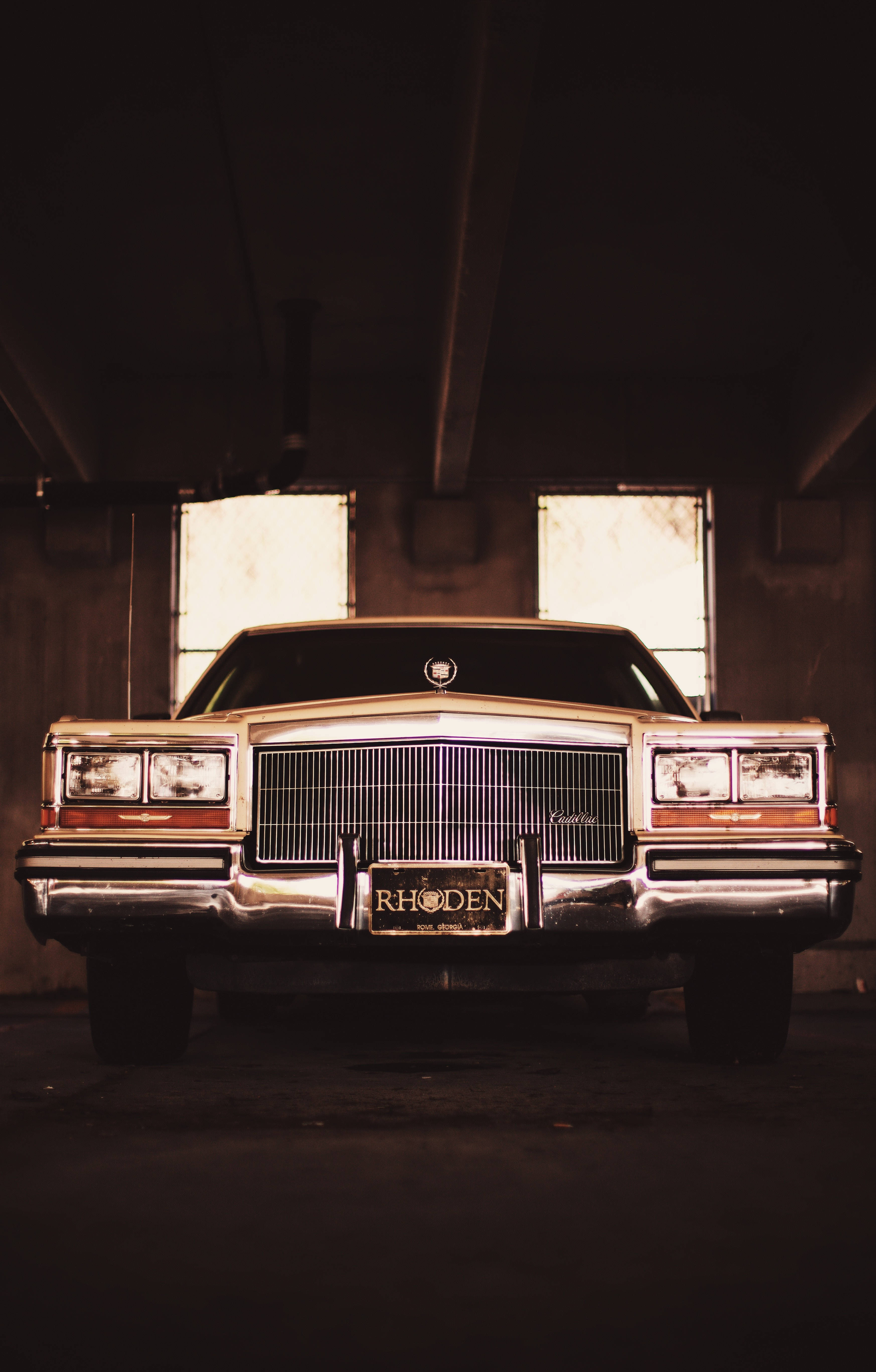 Cadillac 桌布 壁紙 — 一輛復古凱迪拉克轎車在高窗的昏暗混凝土車庫中，在溫暖的燈光下閃閃發光。