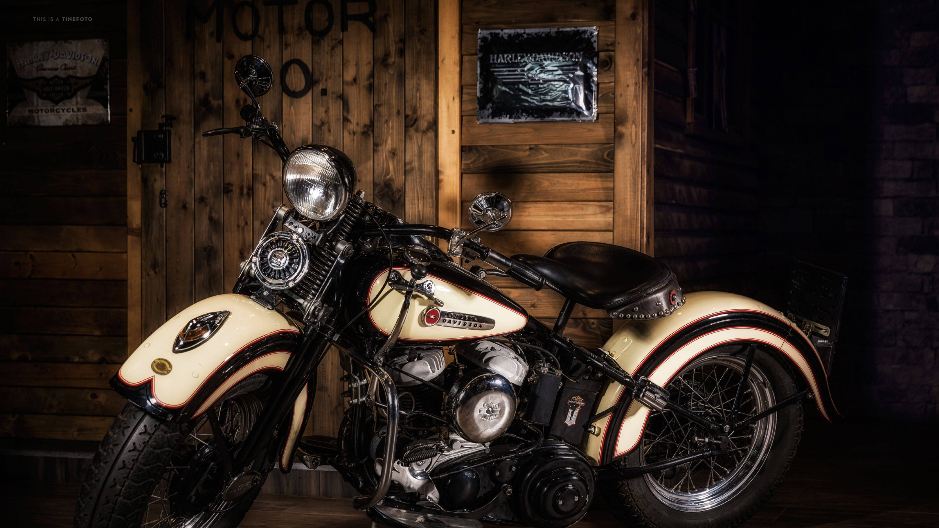 Harley 桌布 壁紙 — 一輛復古奶油色和黑色的Harley-Davidson摩托車在溫暖燈光下於鄉村木車庫中閃耀。
