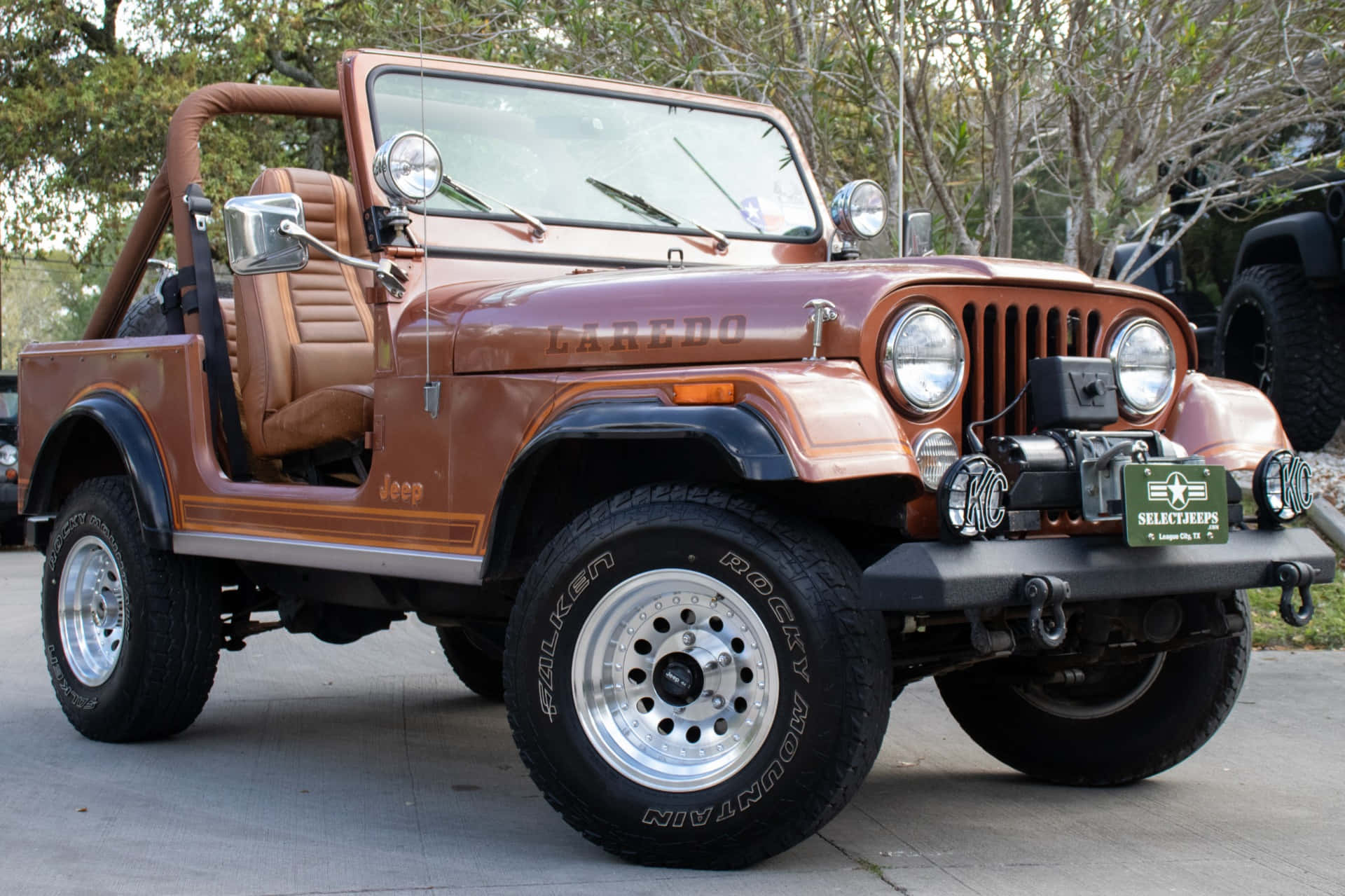 Jeep Cj 桌布 壁紙 — 一輛復古棕色Jeep Wrangler，配備米色內裝和鍍鉻飾邊，停放在樹木環繞的混凝土車道上。