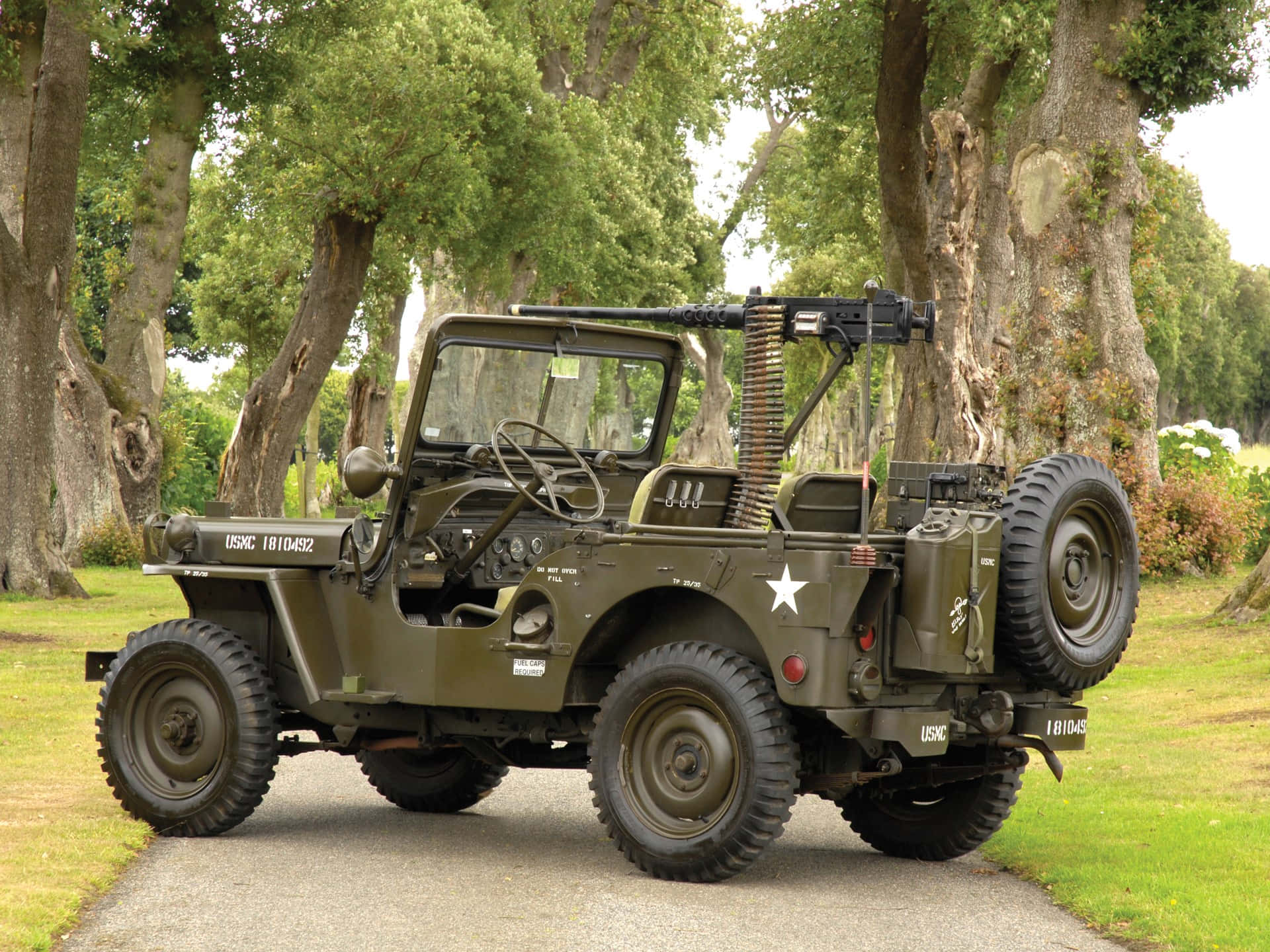 Jeep Willys 桌布 壁紙 — 一輛復古橄欖綠軍用吉普車，裝有機槍，停在大樹下的碎石路上。