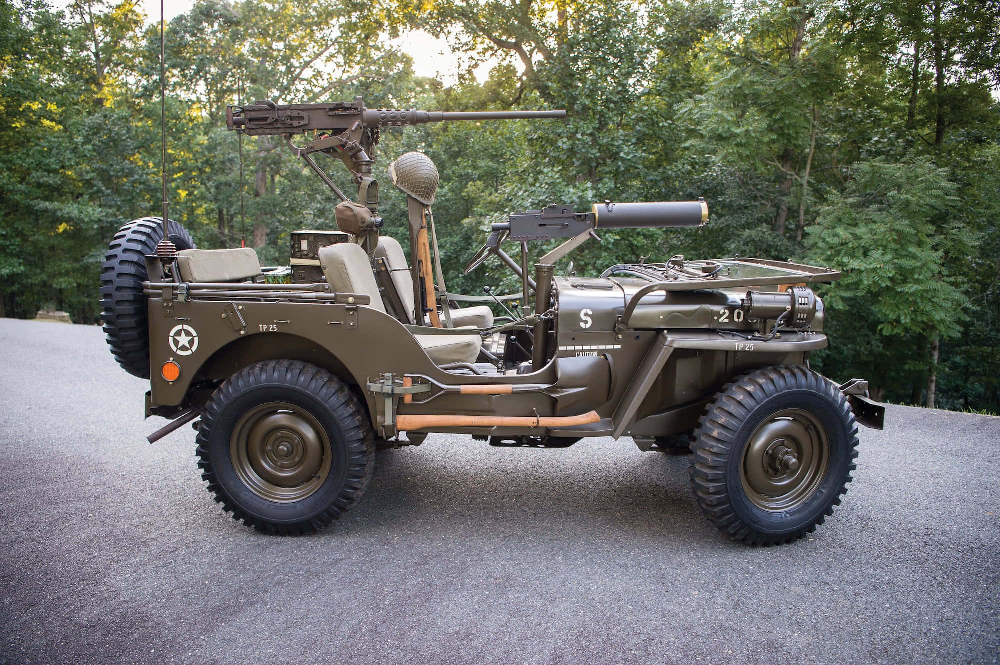 Jeep Willys 桌布 壁紙 — 一輛復古橄欖綠軍用吉普車，裝有機槍，停在碎石地上，周圍是茂密的綠色森林。