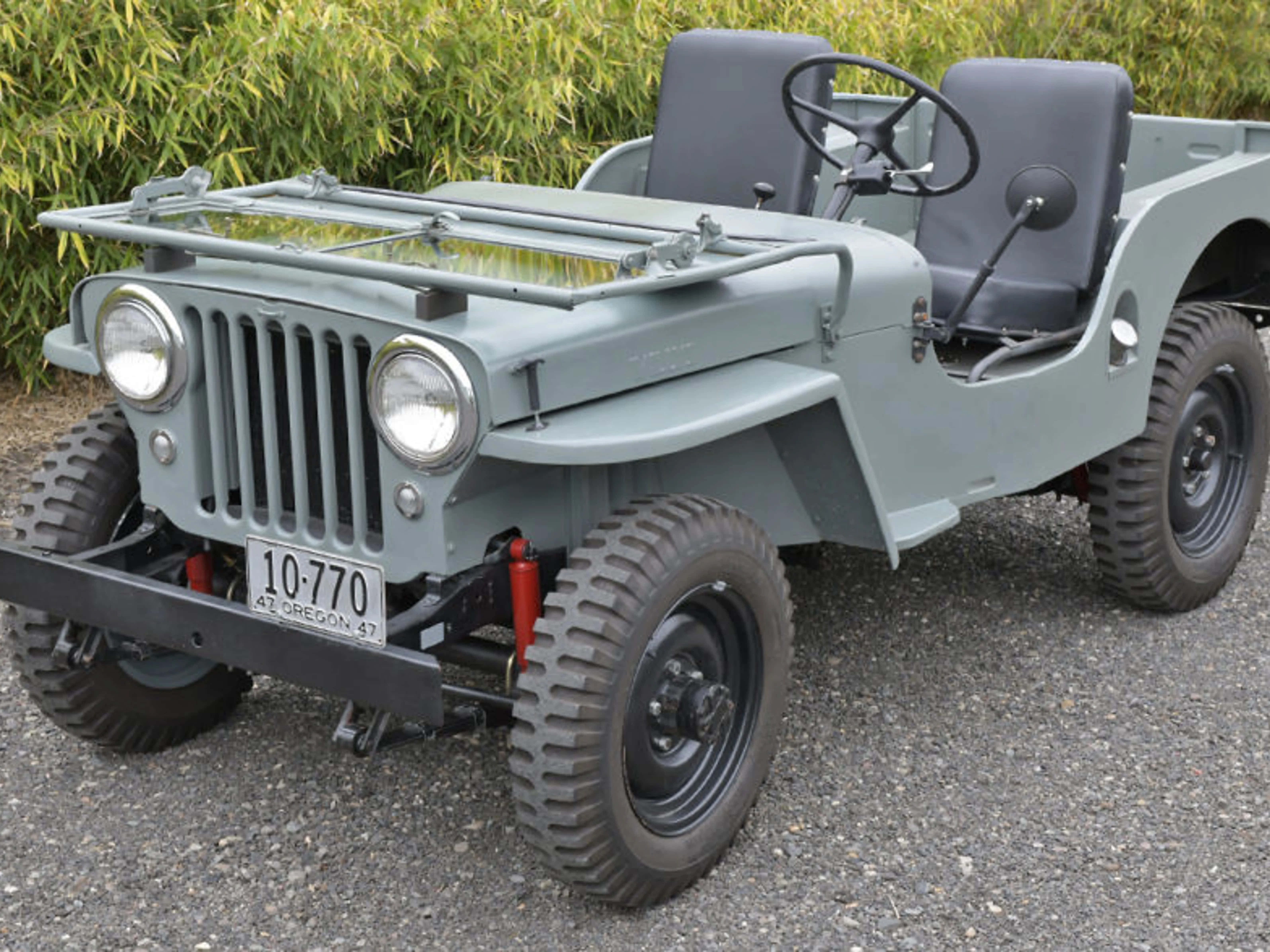 Jeep Willys 桌布 壁紙 — 一輛復古橄欖綠軍用吉普車，配備黑色輪胎和紅色避震器，停在碎石地上，旁邊有綠色竹子。