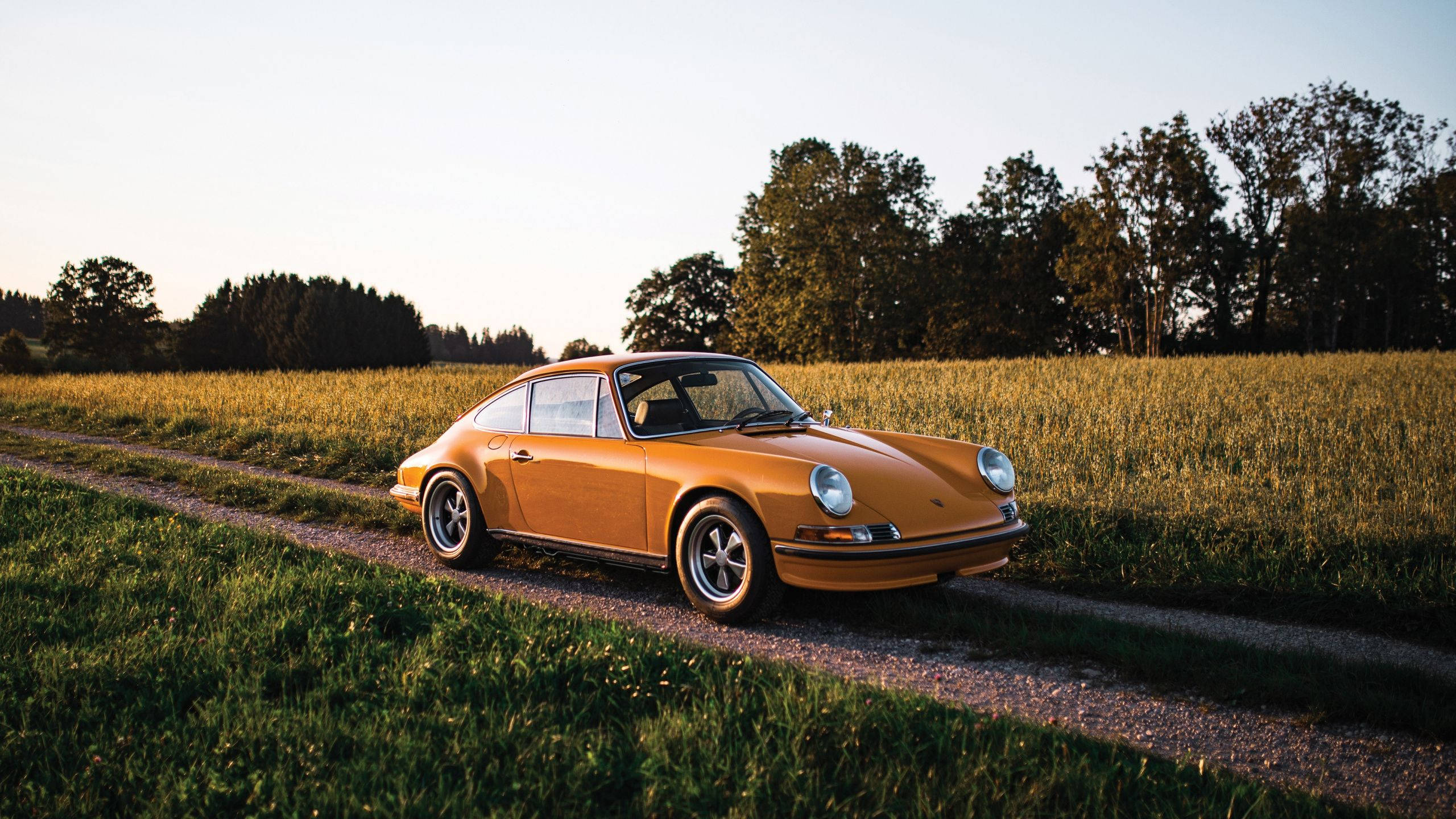 Porsche 911 桌布 壁紙 — 一輛復古橙色保時捷91停在日落時分金色田野旁的碎石路上。