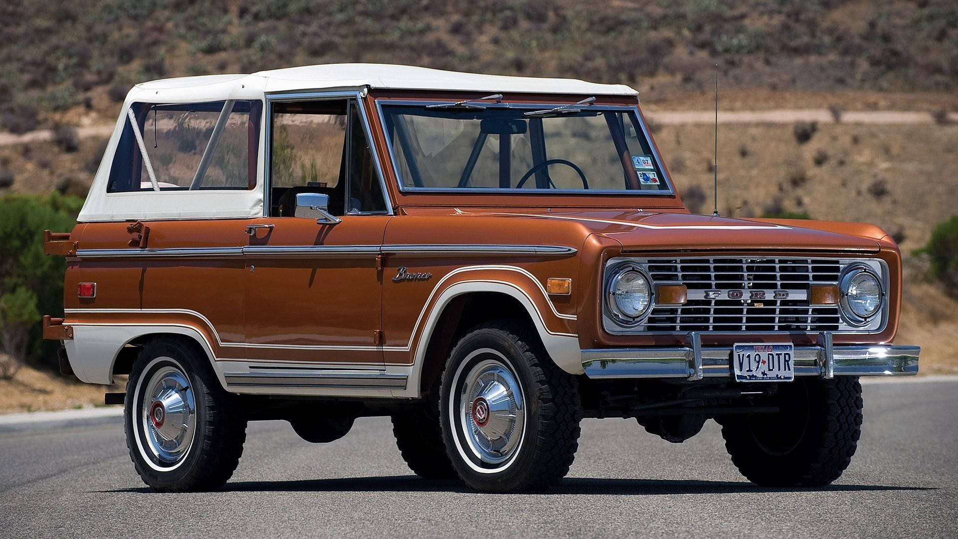 Ford Bronco 桌布 壁紙 — 一輛復古橙色和白色的福特Bronco，帶有鍍鉻裝飾，停在沙漠公路上，陽光普照。