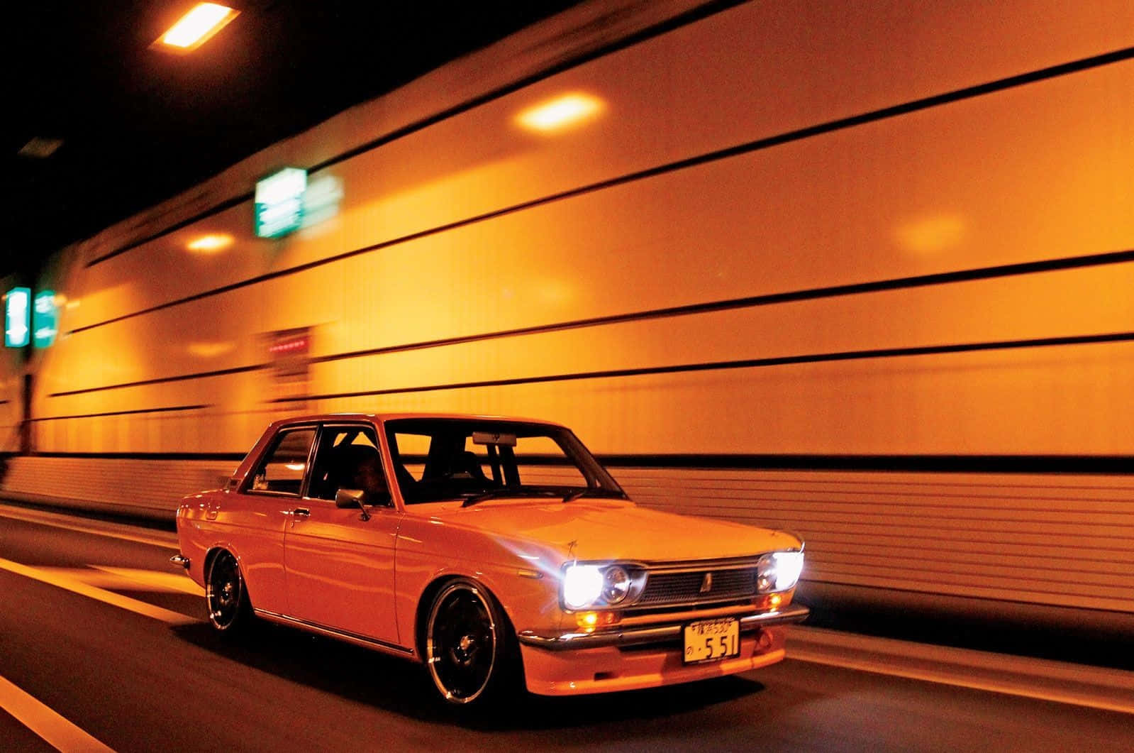 Datsun 桌布 壁紙 — 一輛復古橙色轎車在夜間高速穿過隧道，車頭燈閃爍，牆壁因運動而模糊。