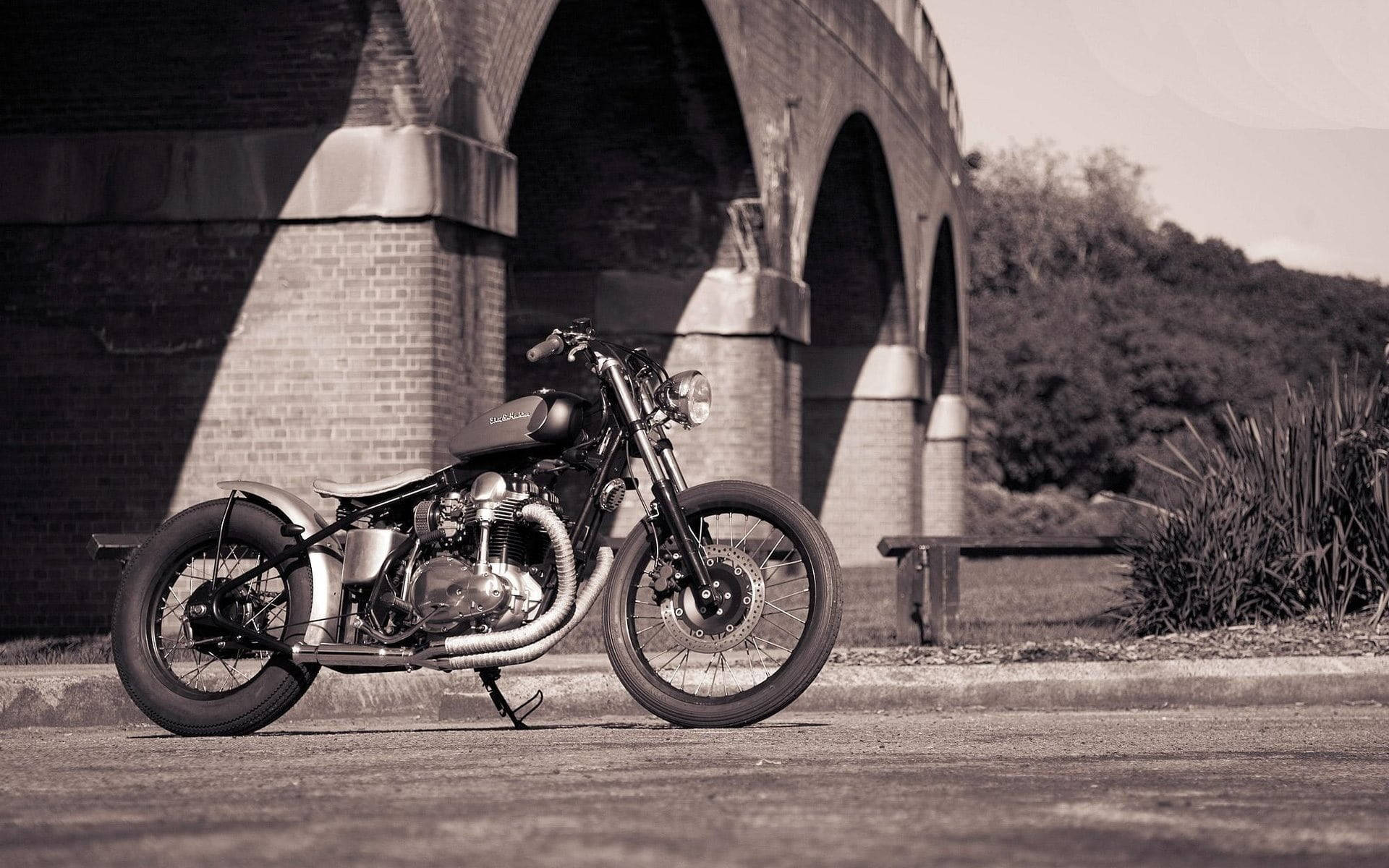 Bobber 桌布 壁紙 — 一輛復古機車停泊在石橋下，帶有懷舊棕色調和柔和陰影。