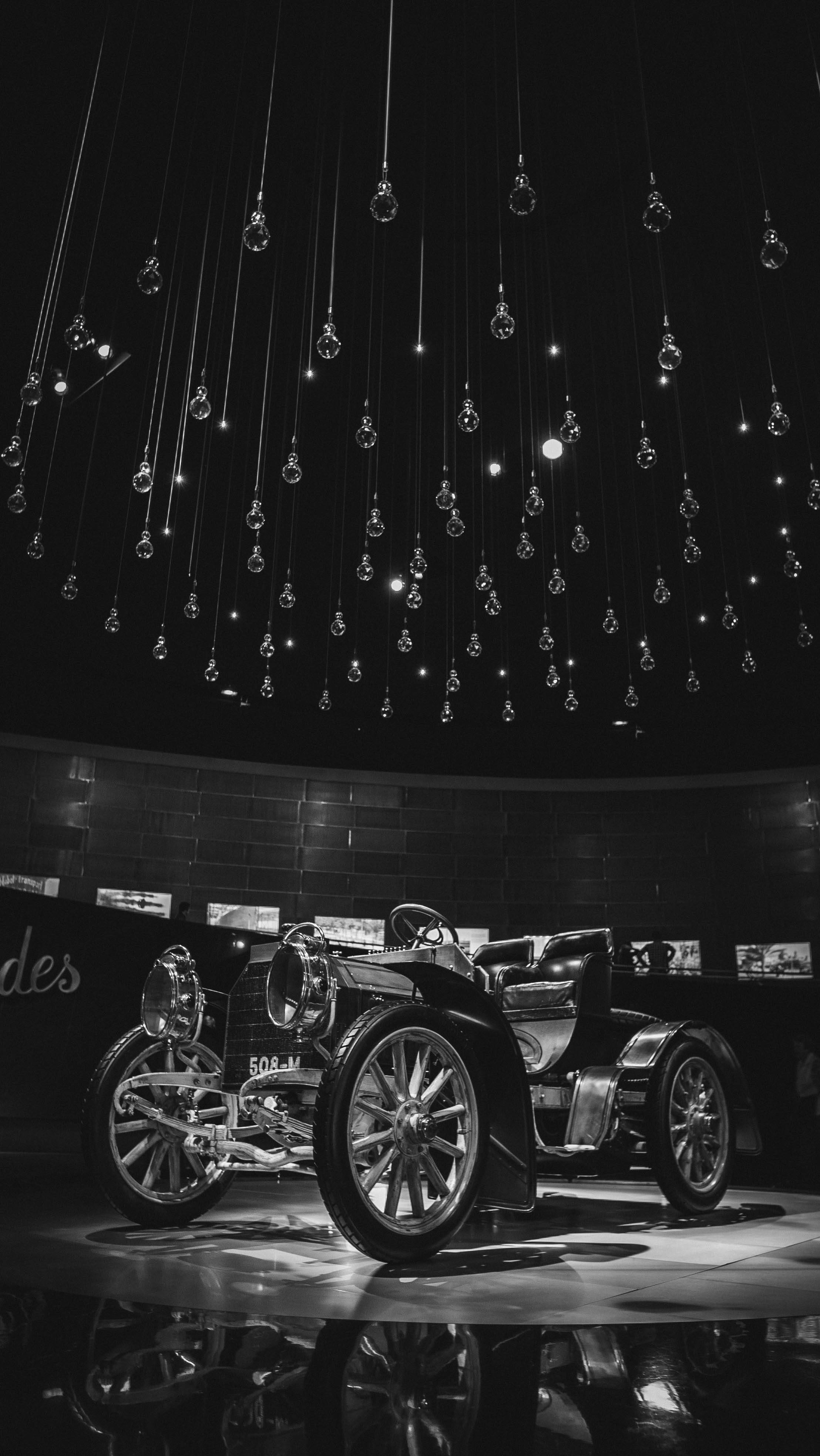 Mercedes Amg 桌布 壁紙 — 一輛復古汽車在單色博物館展覽中，在懸掛的玻璃燈泡下閃閃發光，地板具有反射效果。
