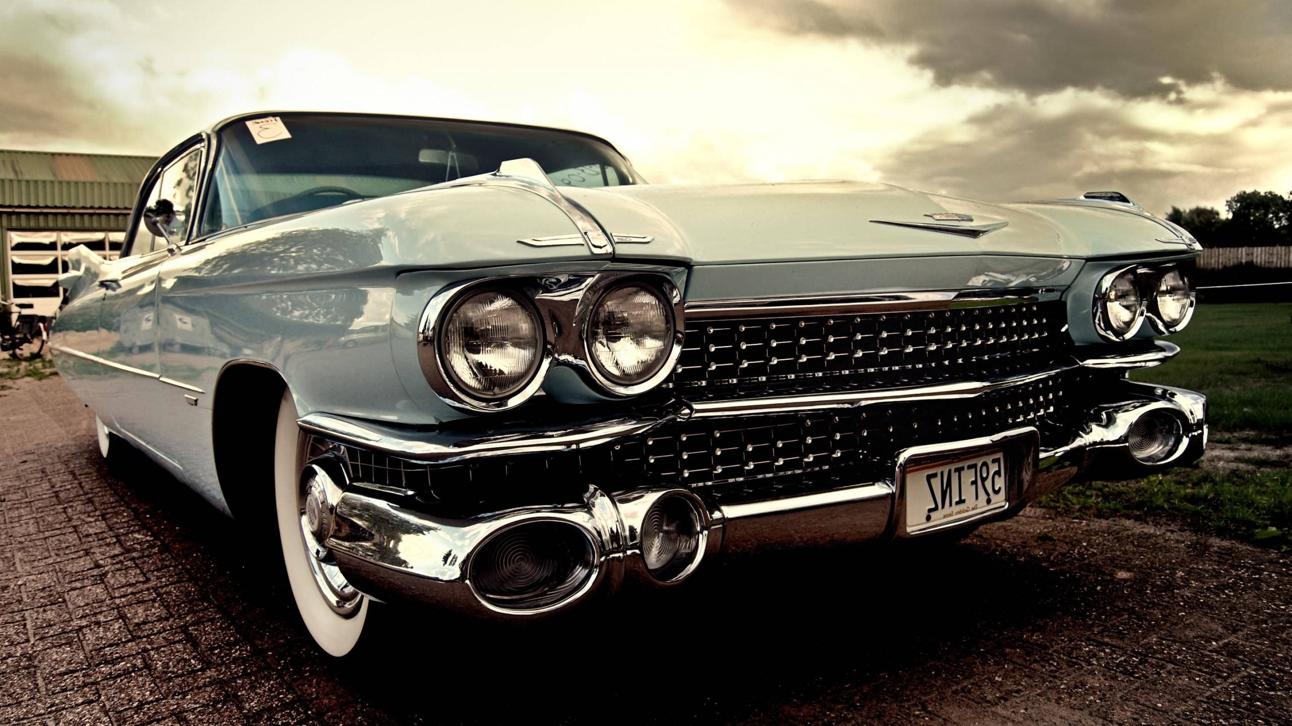 Cadillac 桌布 壁紙 — 一輛復古淺藍色凱迪拉克，帶有鍍鉻細節和白色輪胎，停在鵝卵石車道上，天空多雲，氣氛戲劇化。