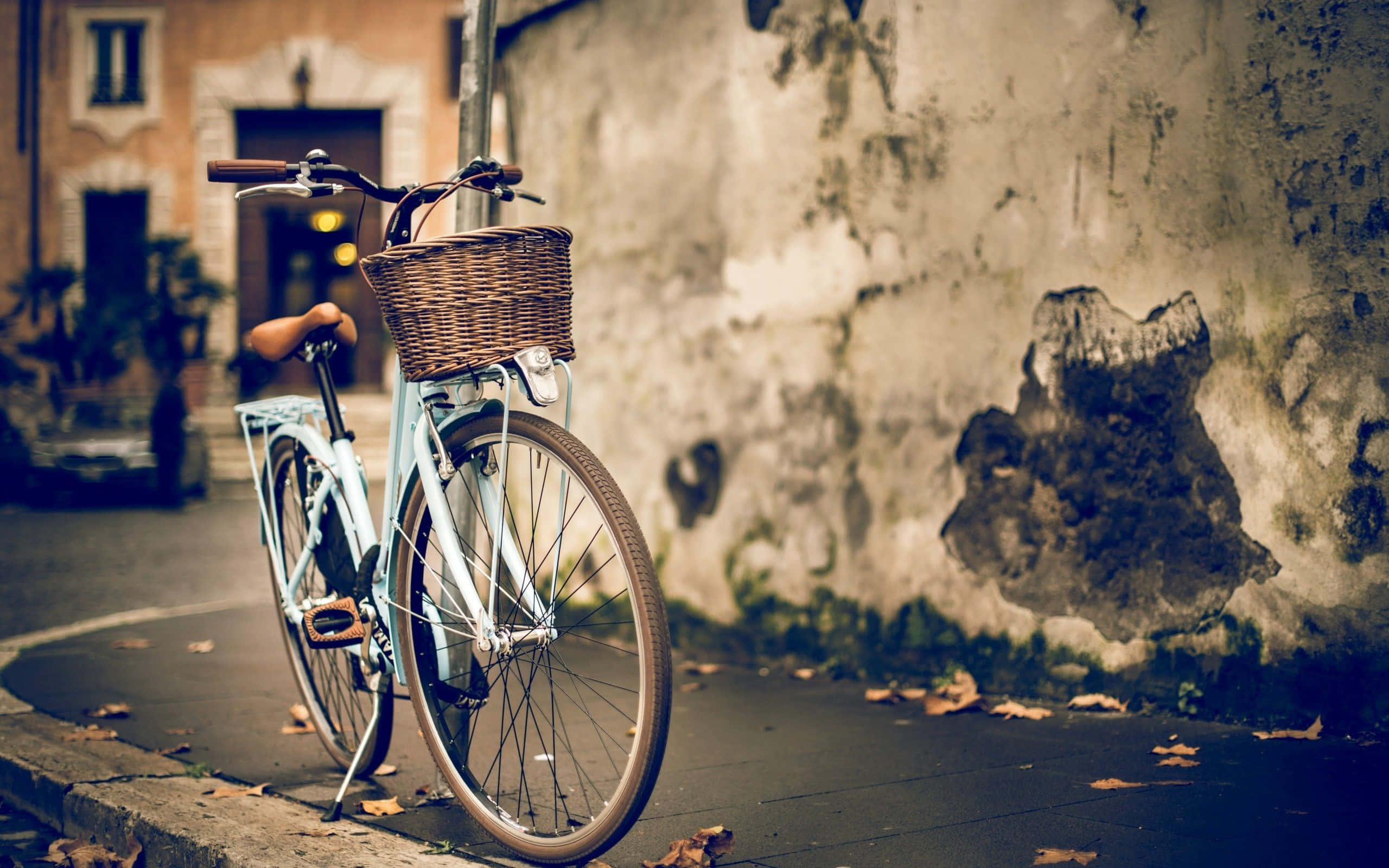 Bicycle 桌布 壁紙 — 一輛復古淺藍色腳踏車，配有柳條籃，倚靠在寧靜秋日街道上風化的牆壁上。