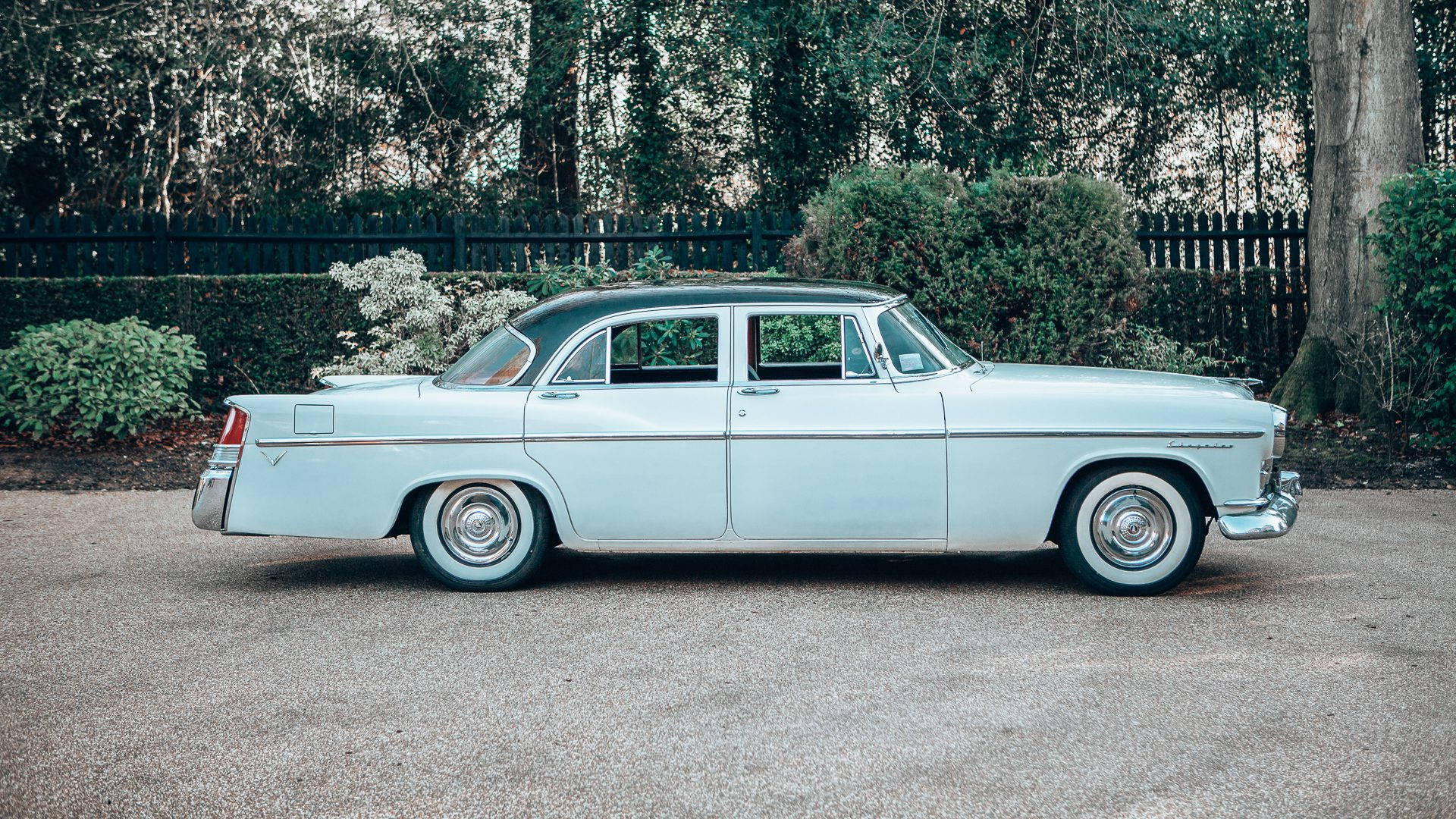Chrysler 桌布 壁紙 — 一輛復古淺藍色轎車，黑色車頂，停在碎石路上，旁邊是深色圍欄和綠植。
