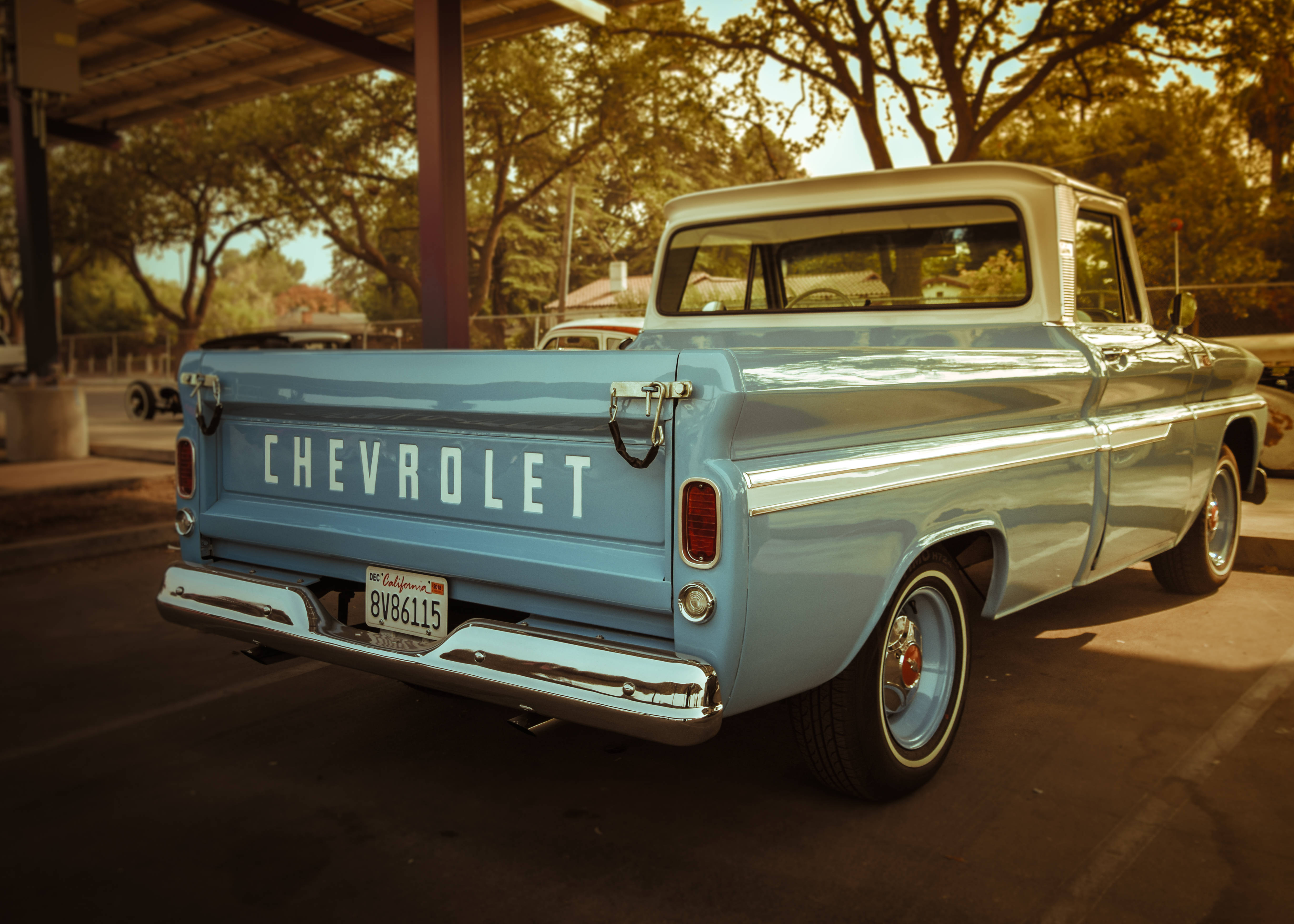 Chevrolet 桌布 壁紙 — 一輛復古淺藍色雪佛蘭皮卡車在溫暖的金色陽光下閃閃發光，停放在有樹木背景的遮陽篷下。