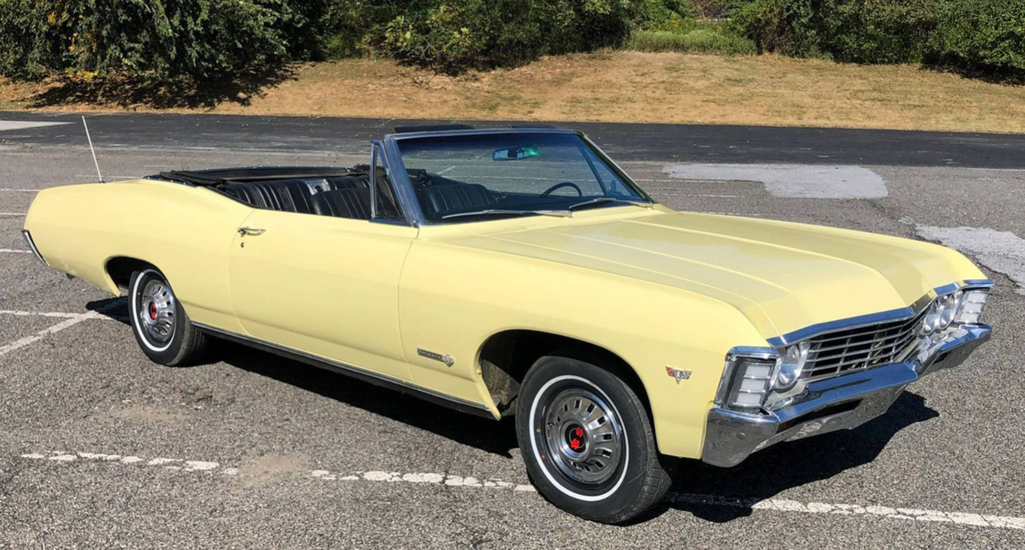 chevrolet impala 1967 桌布 壁紙 — 一輛復古淺黃色敞篷跑車停放在陽光明媚的瀝青停車場，背景有綠色灌木叢。