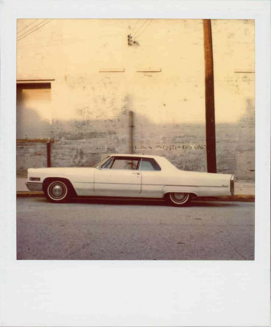 Aesthetic Polaroid 桌布 壁紙 — 一輛復古白色凱迪拉克Coupe de Ville停泊在粗糙的街道上，旁邊是風化的牆壁，沐浴在溫暖的金色光線下。