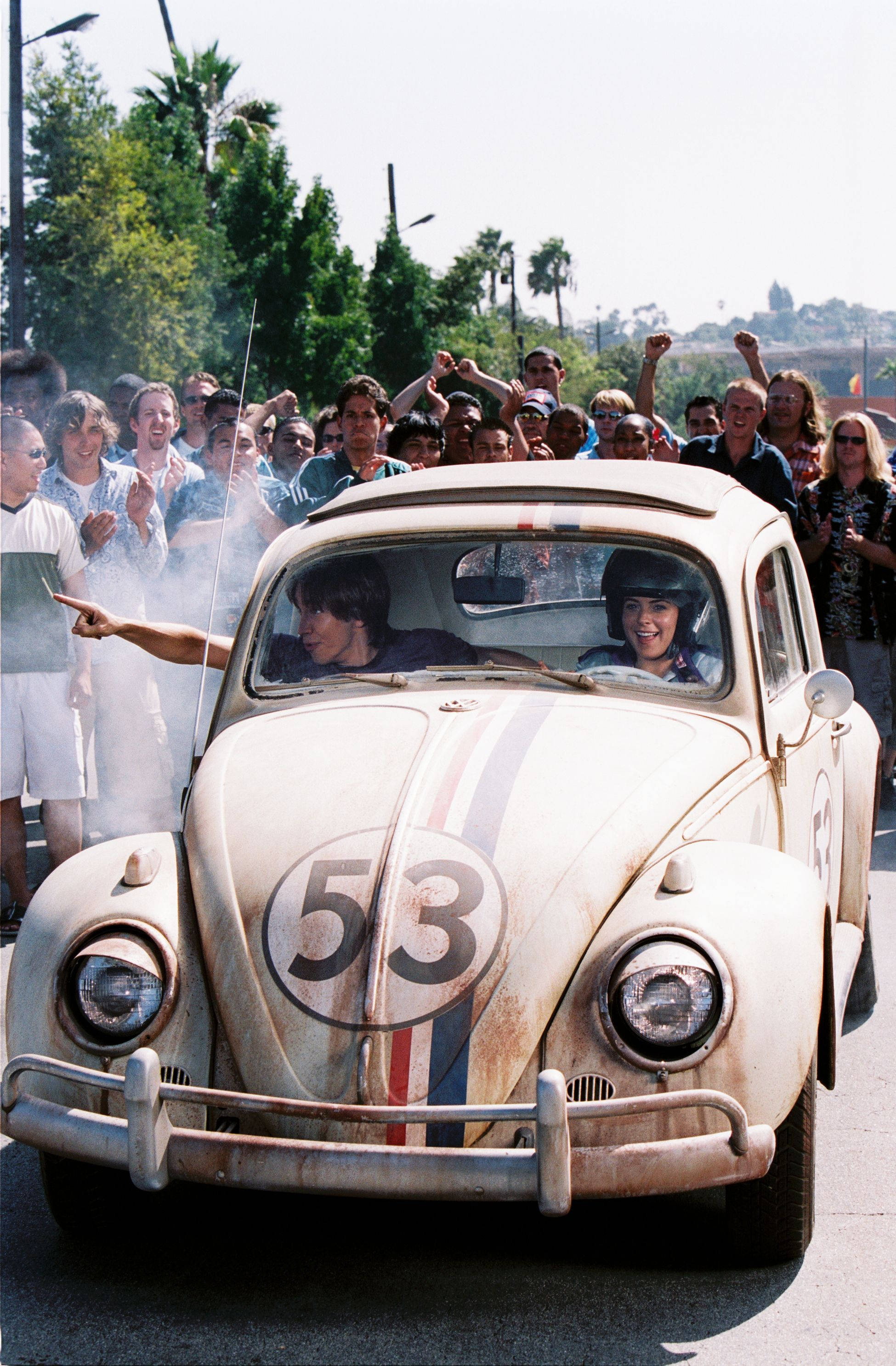 Herbie 桌布 壁紙 — 一輛復古白色福斯金龜車（編號53）在陽光明媚的街道上奔馳，受到熱鬧人群的歡呼。