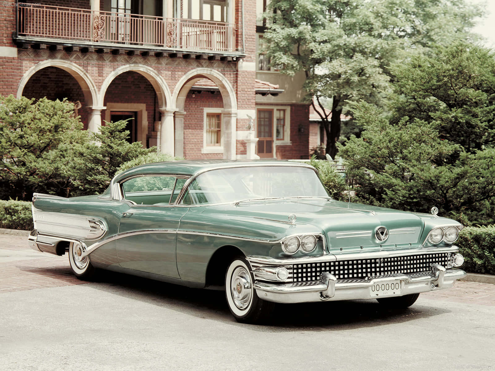 Vintage Car 桌布 壁紙 — 一輛復古的綠色和白色1950年代凱迪拉克停在一棟紅磚建築前，建築有拱形門口和茂密的綠樹。